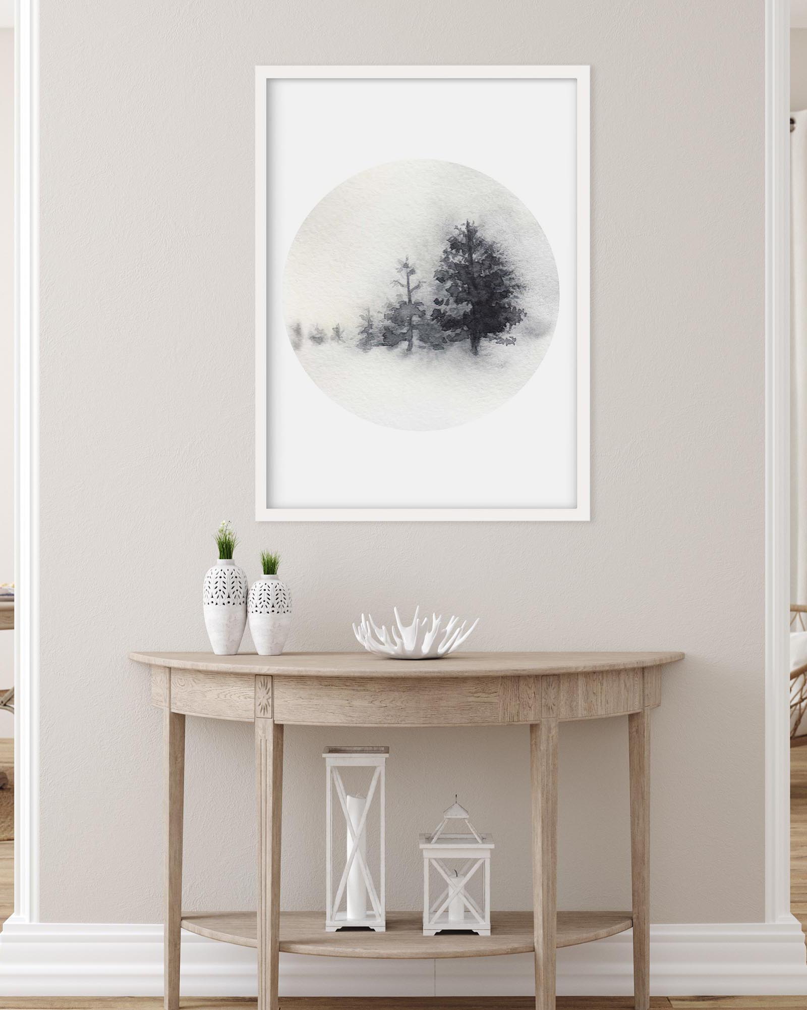 Framed artwork of trees in a snowy landscape on a wall above a wooden console table.