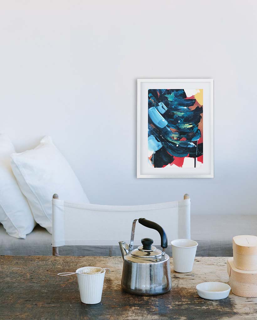 Framed abstract art on a wall above a wooden table with kitchen items.