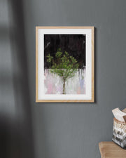 Framed artwork of a tree on a gray wall with a basket on a chair below.