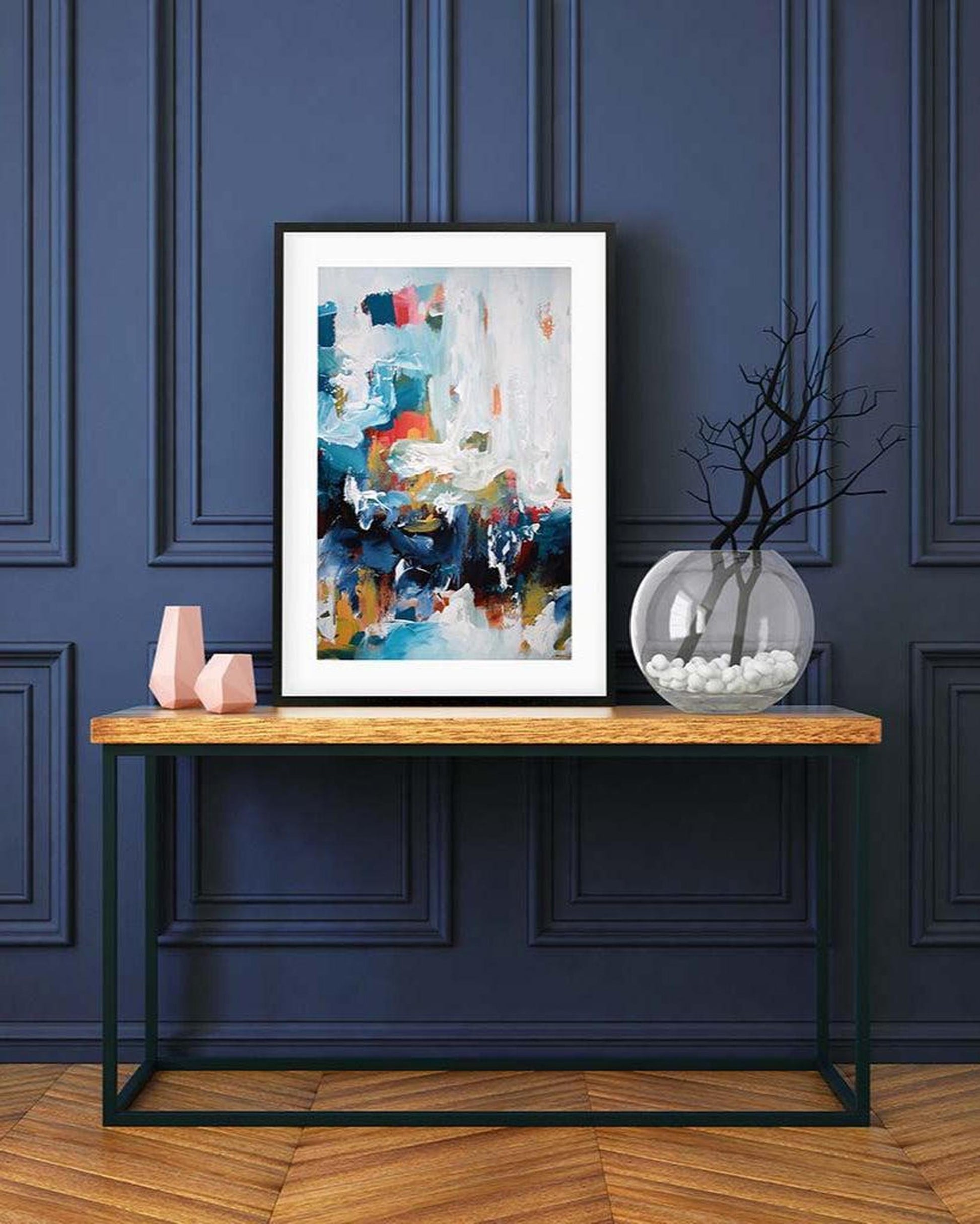 Framed abstract art on a wooden console table against a dark blue paneled wall.