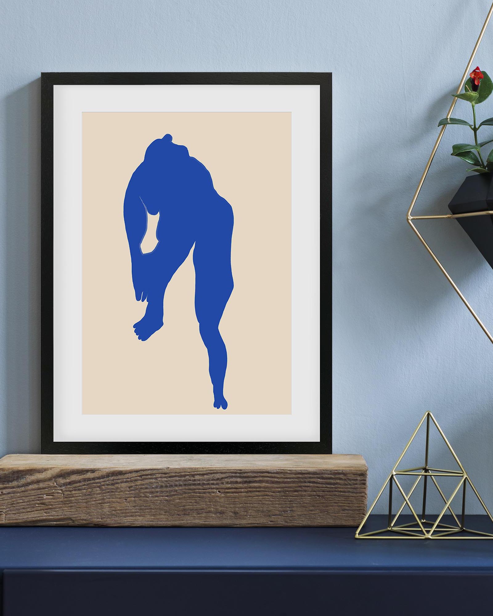 Framed artwork with a blue silhouette on a beige background, displayed on a shelf against a light blue wall.