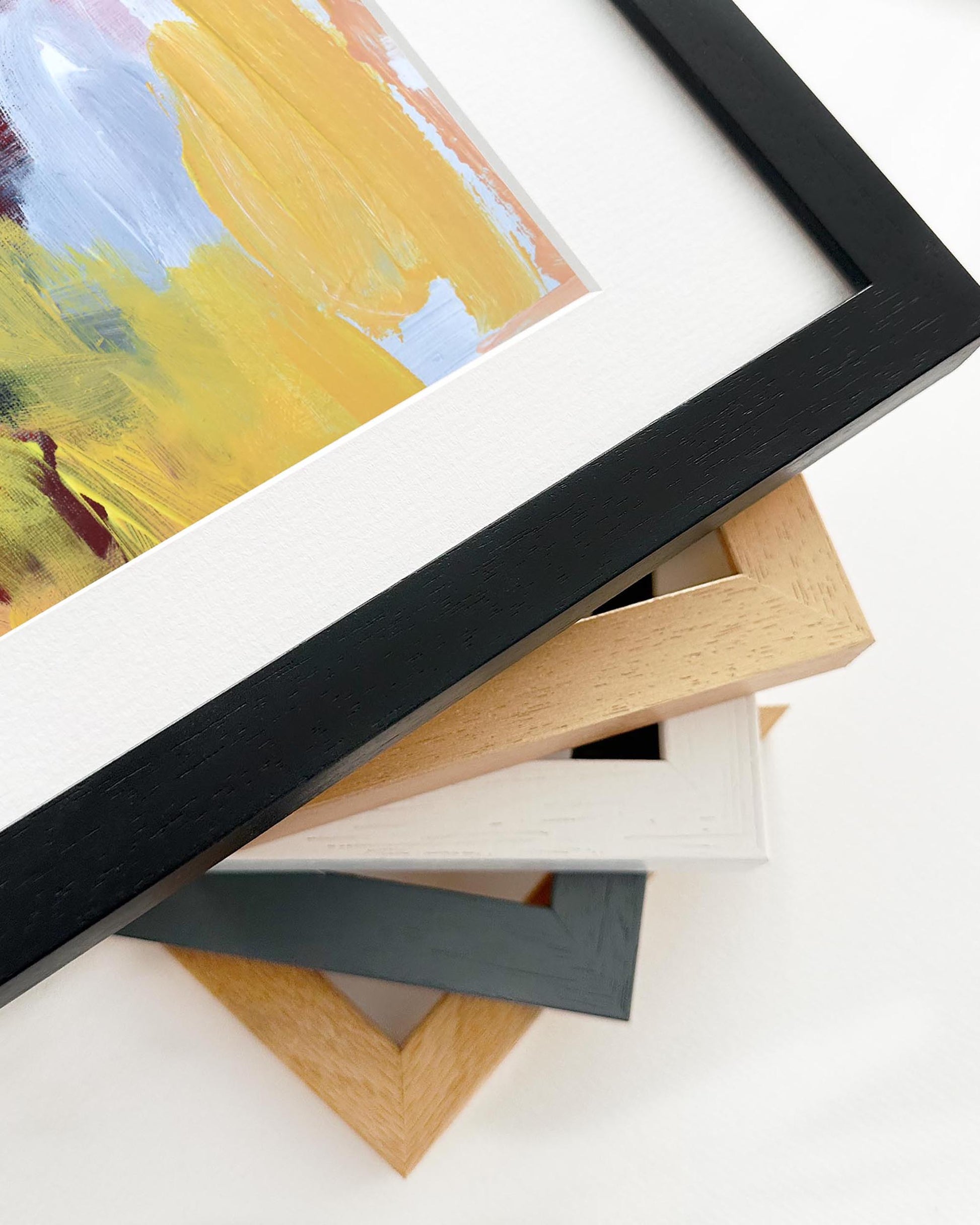 Stack of various picture frames on a white surface with a partially visible painting.