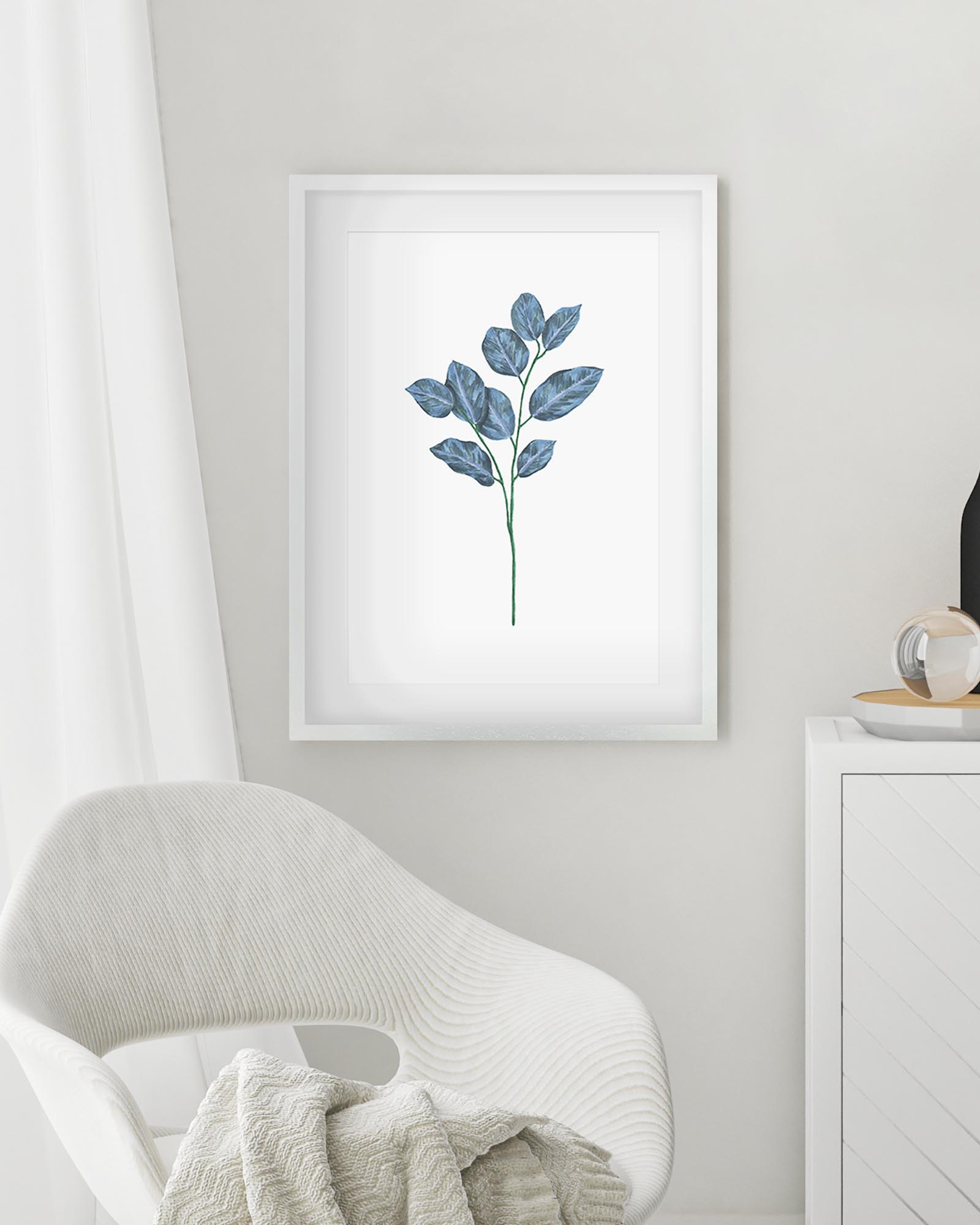 Framed botanical print of blue leaves on a white wall above a white chair.