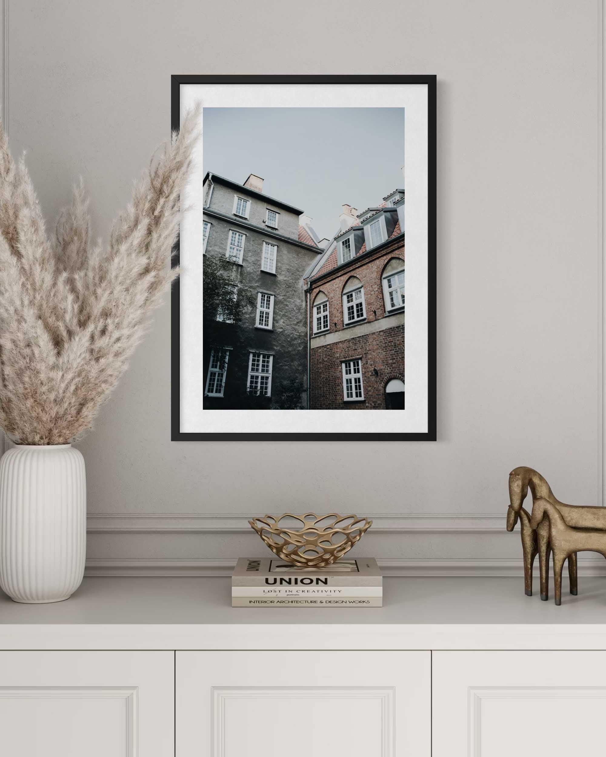 Framed photograph of a building on a wall above a white cabinet with decorative items.