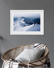 Framed photograph of a snowy mountain landscape on a gray wall above a wicker chair with a cushion.