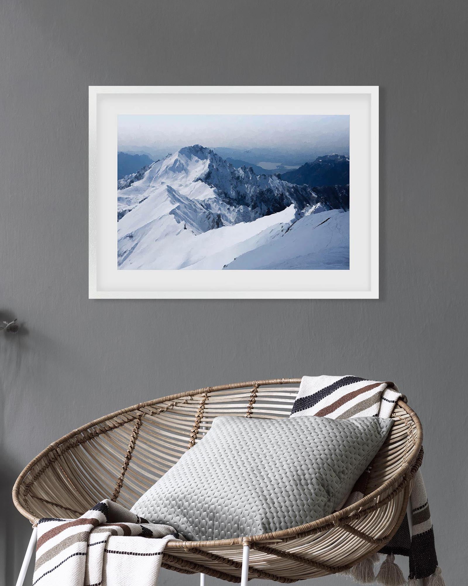 Framed photograph of a snowy mountain landscape on a gray wall above a wicker chair with a cushion.
