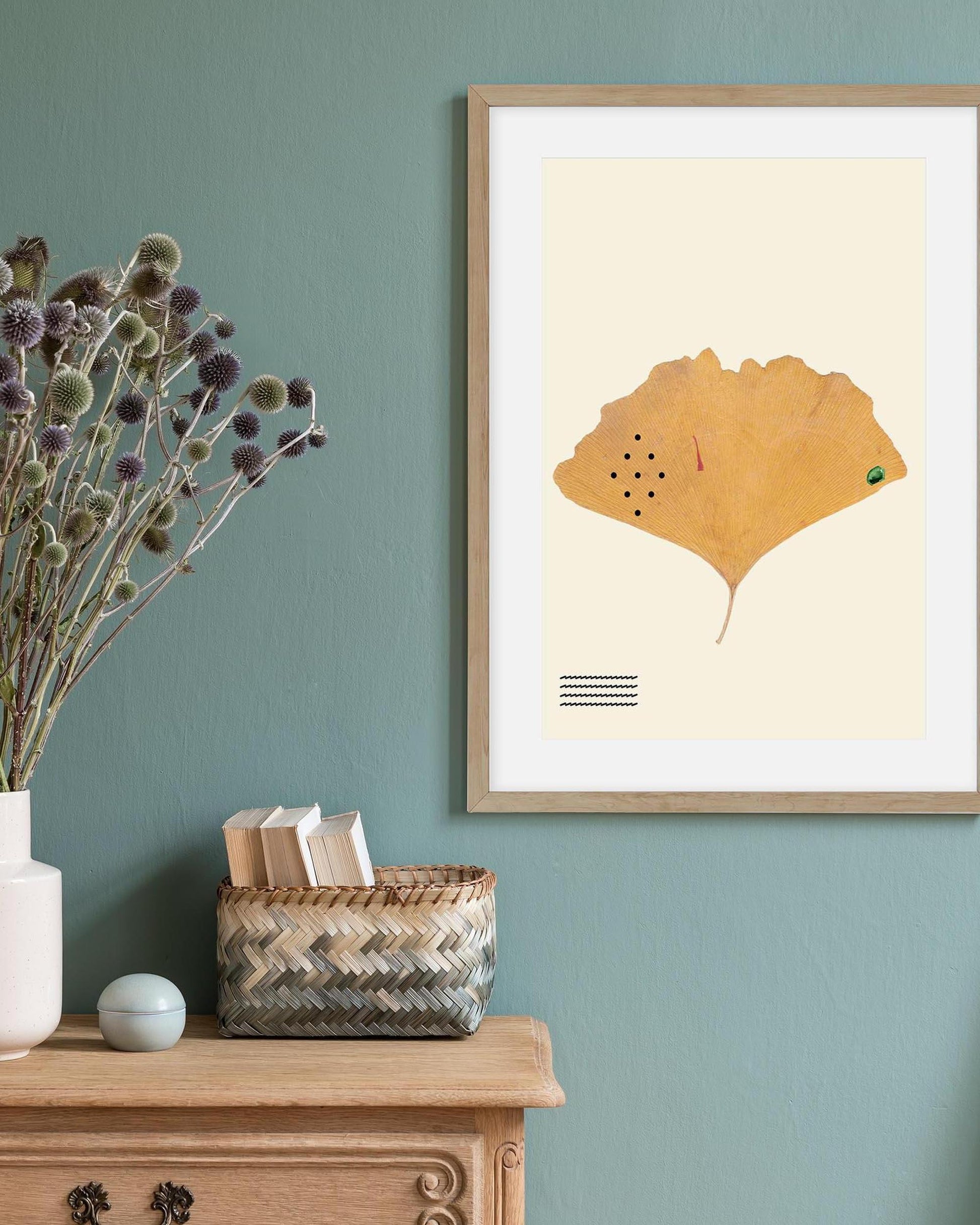 Framed artwork of a leaf on a wall with a wooden cabinet and decorative items.