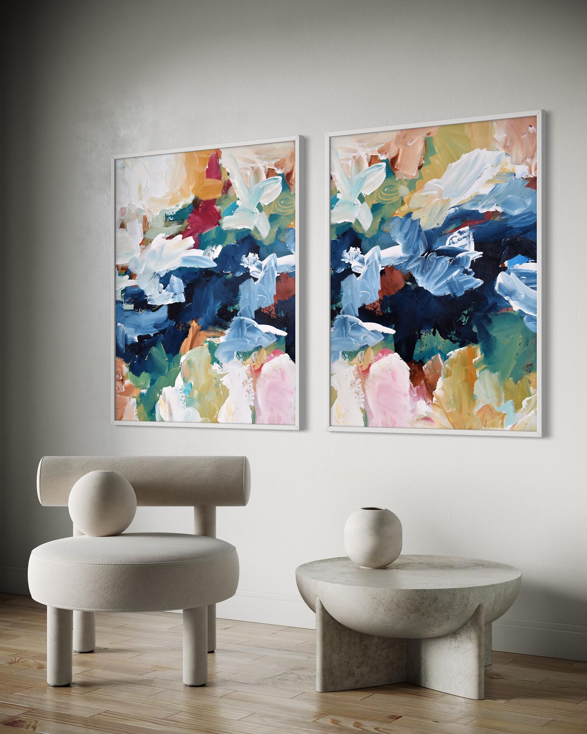Two abstract paintings on a wall with a modern chair and table below.