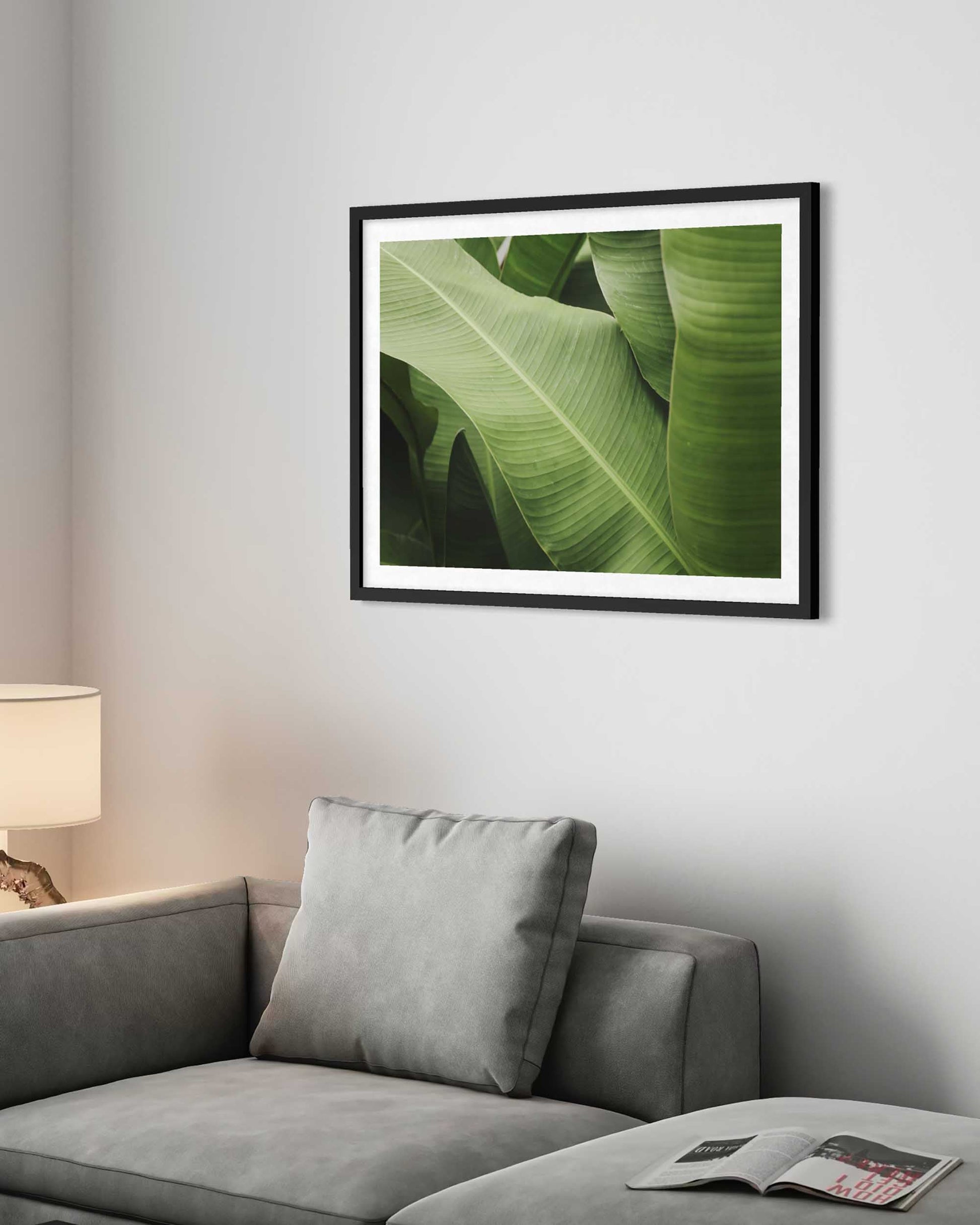 Framed artwork of green leaves on a wall above a gray sofa.