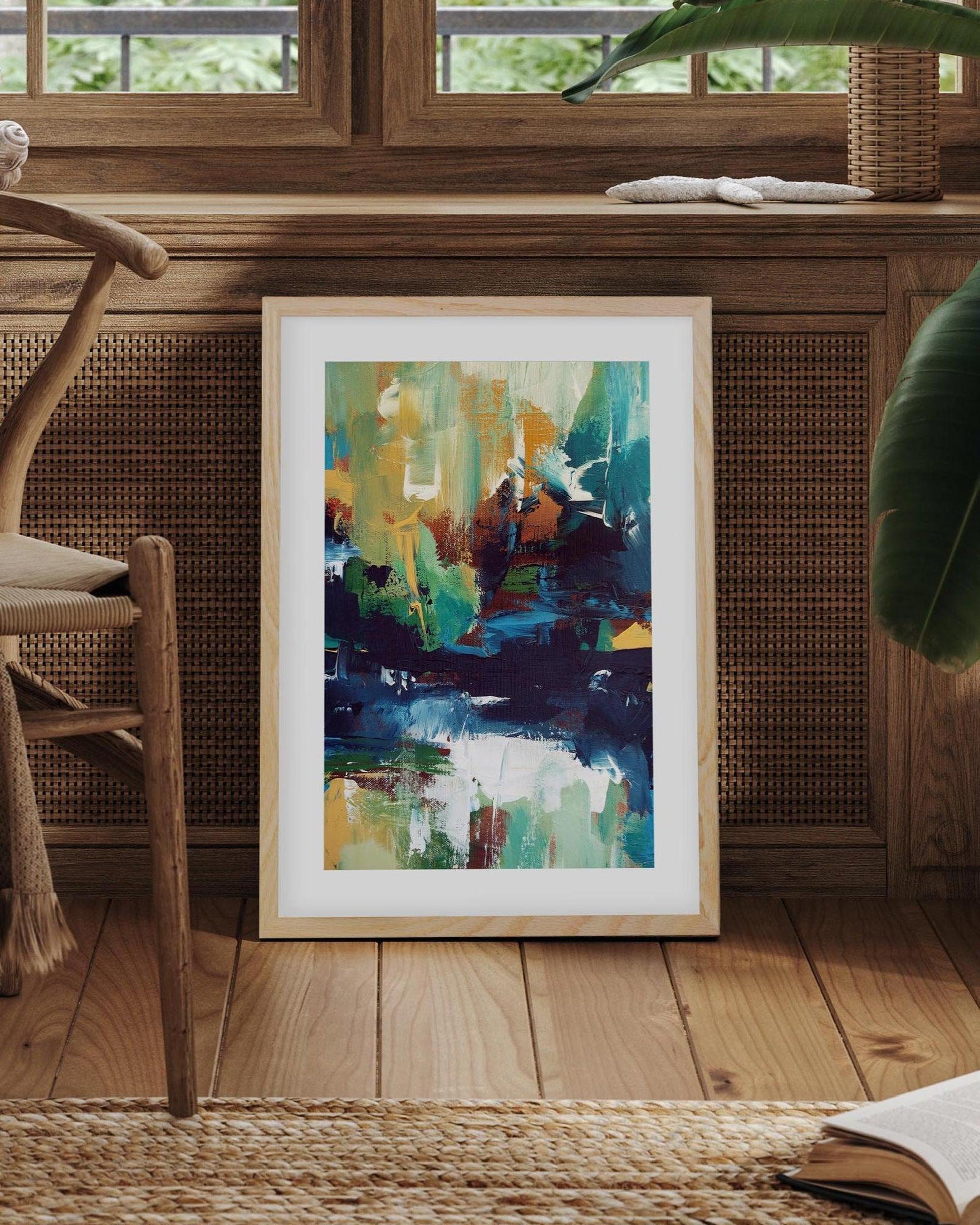 Framed abstract art on a wooden floor with a chair and books in a cozy room.