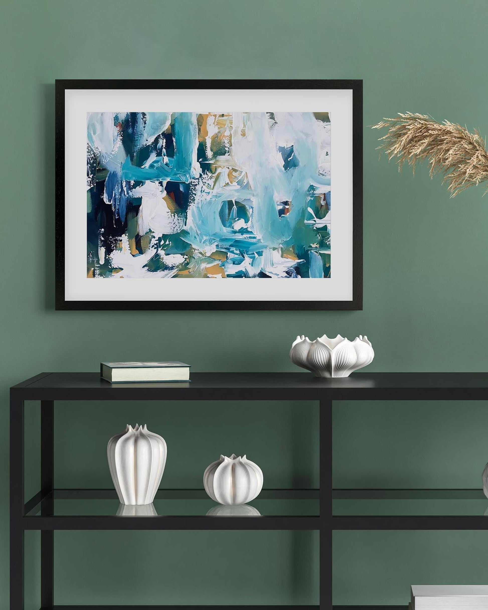 Framed abstract art piece on a green wall with decorative items on a shelf below.