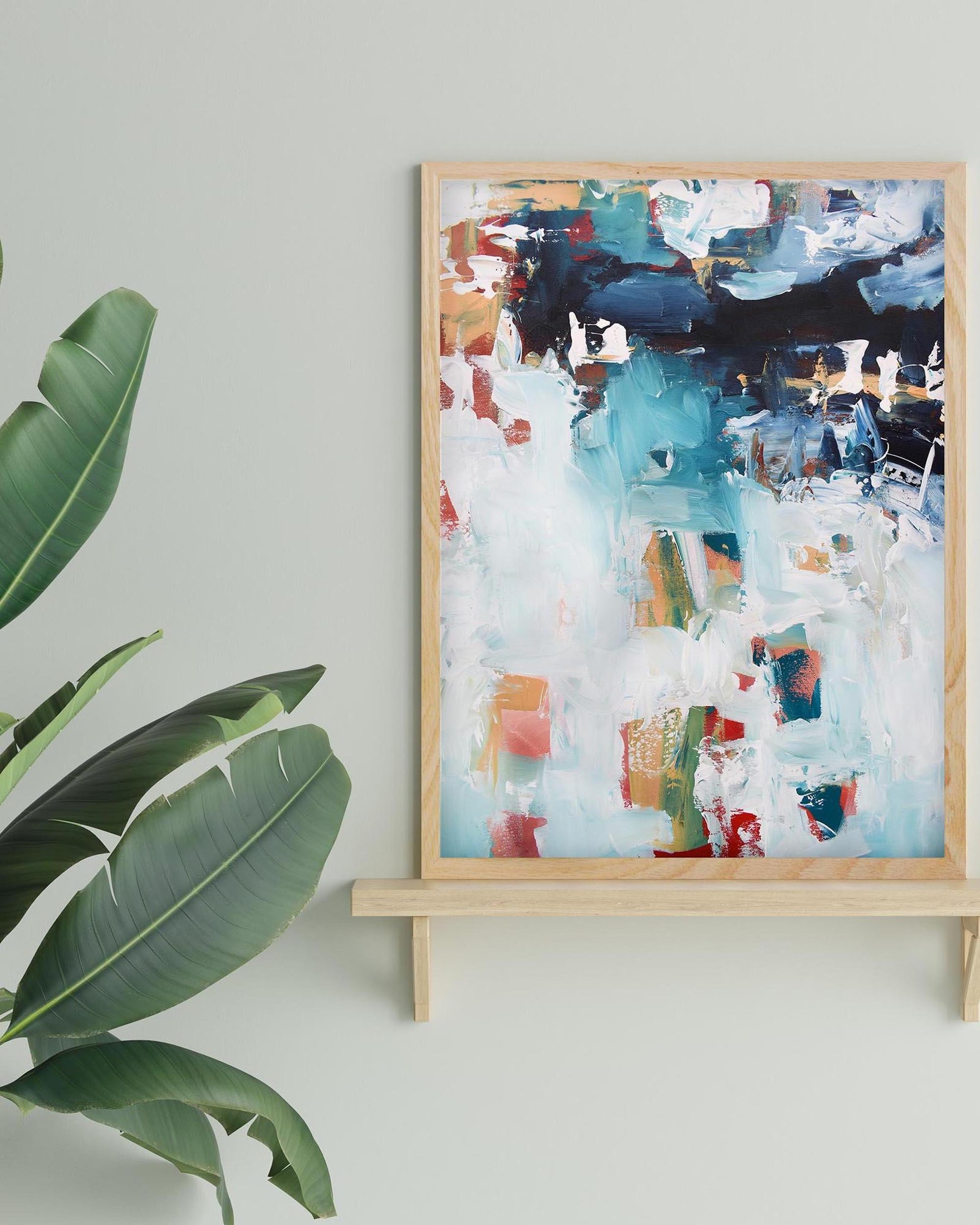 Abstract painting in a wooden frame on a stand with a plant to the left.