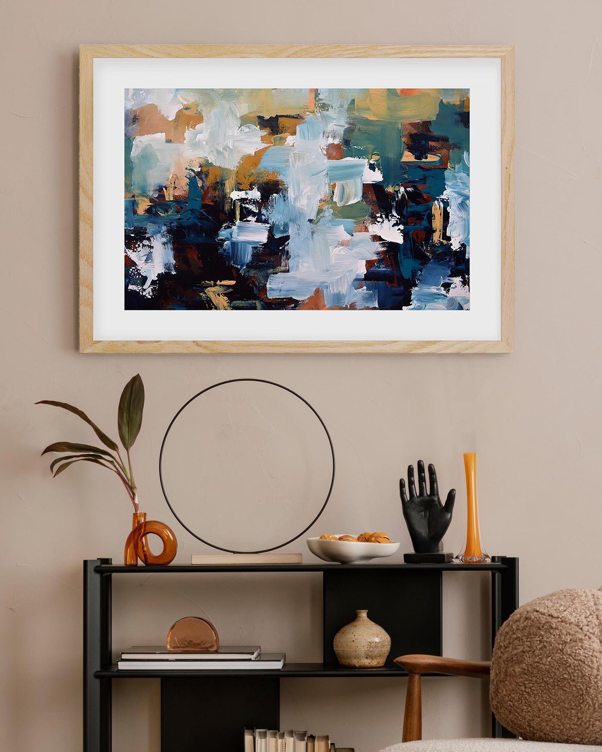 Abstract painting in a wooden frame on a wall above a shelf with decorative items.