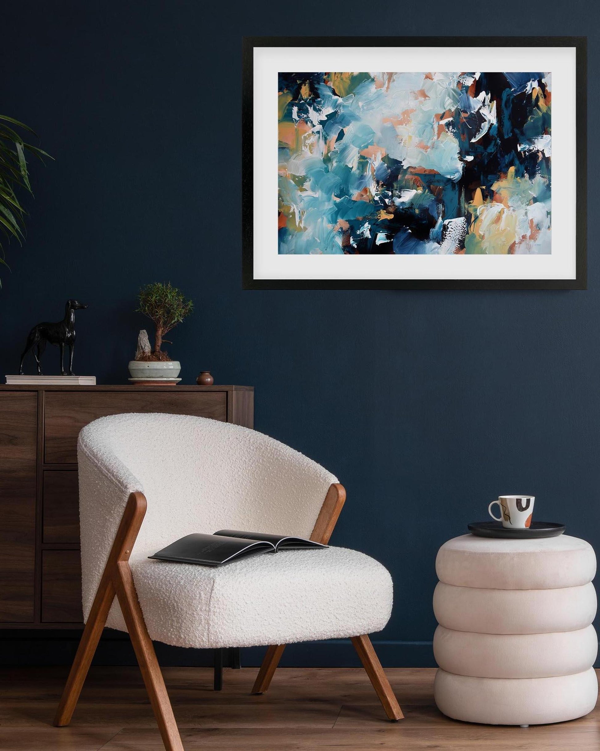 Modern interior with a white armchair, side table, and abstract painting on a dark blue wall.