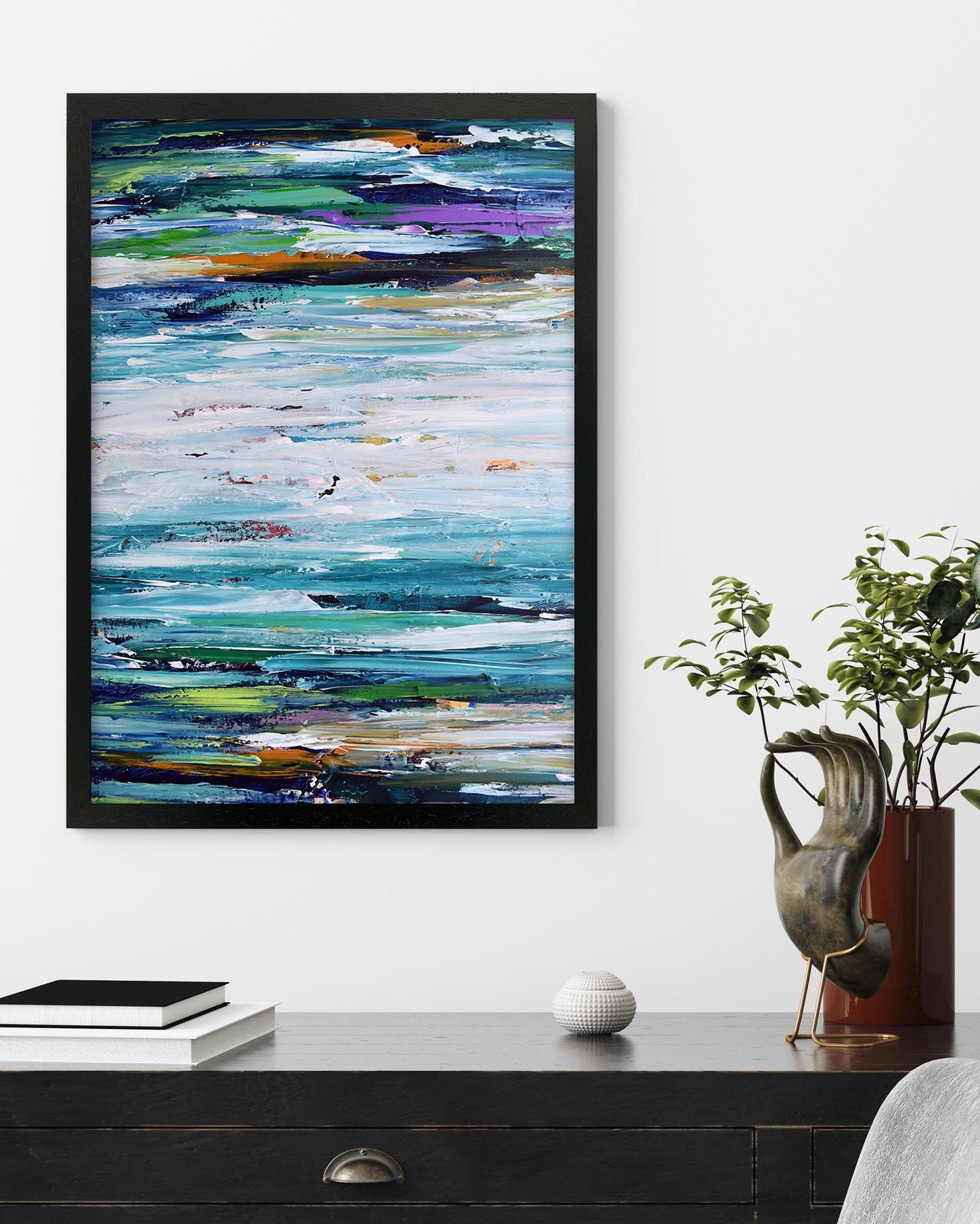 Abstract painting with colorful brushstrokes in a black frame on a wall above a desk.