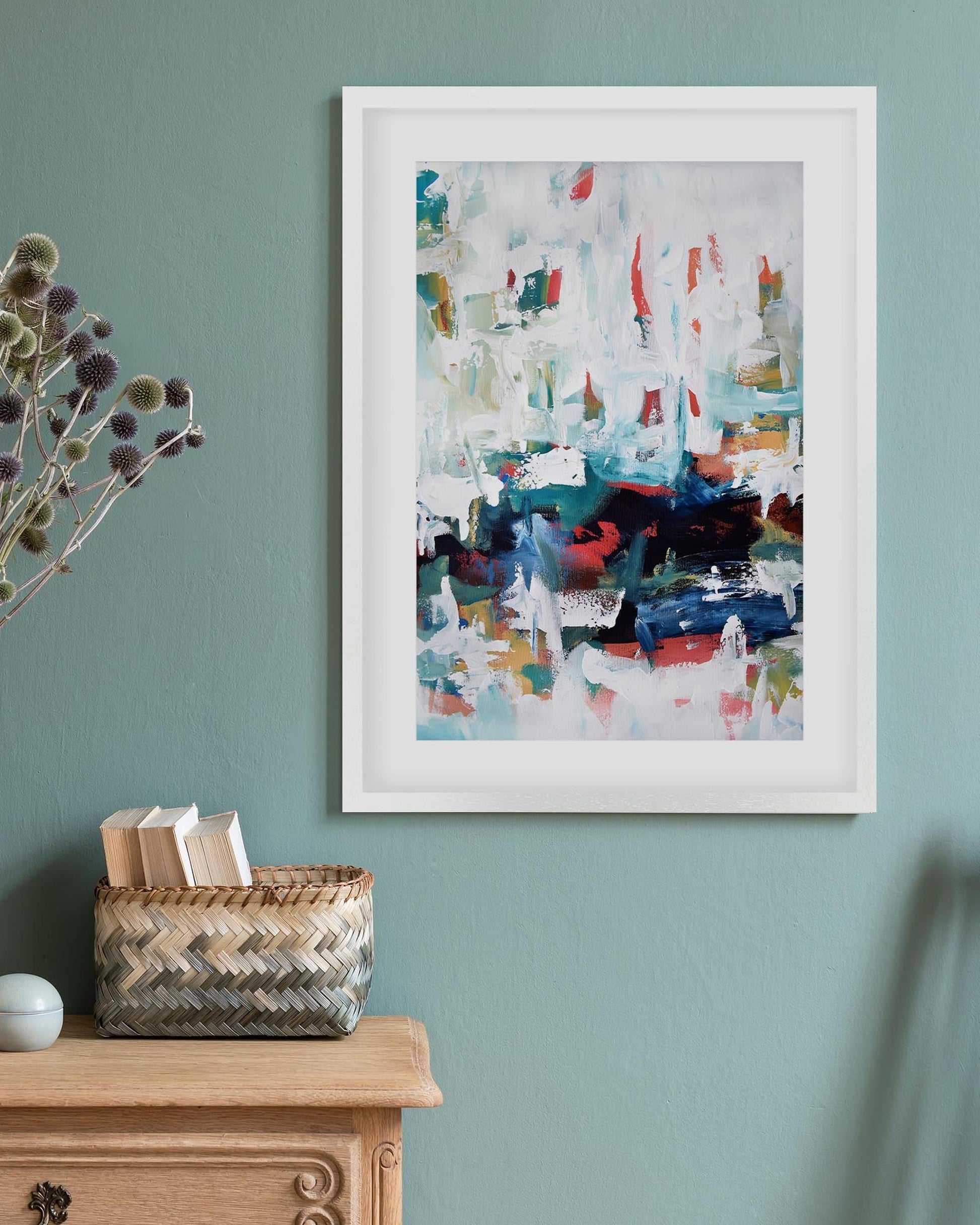 Framed abstract art on a wall with a wooden cabinet and basket below.