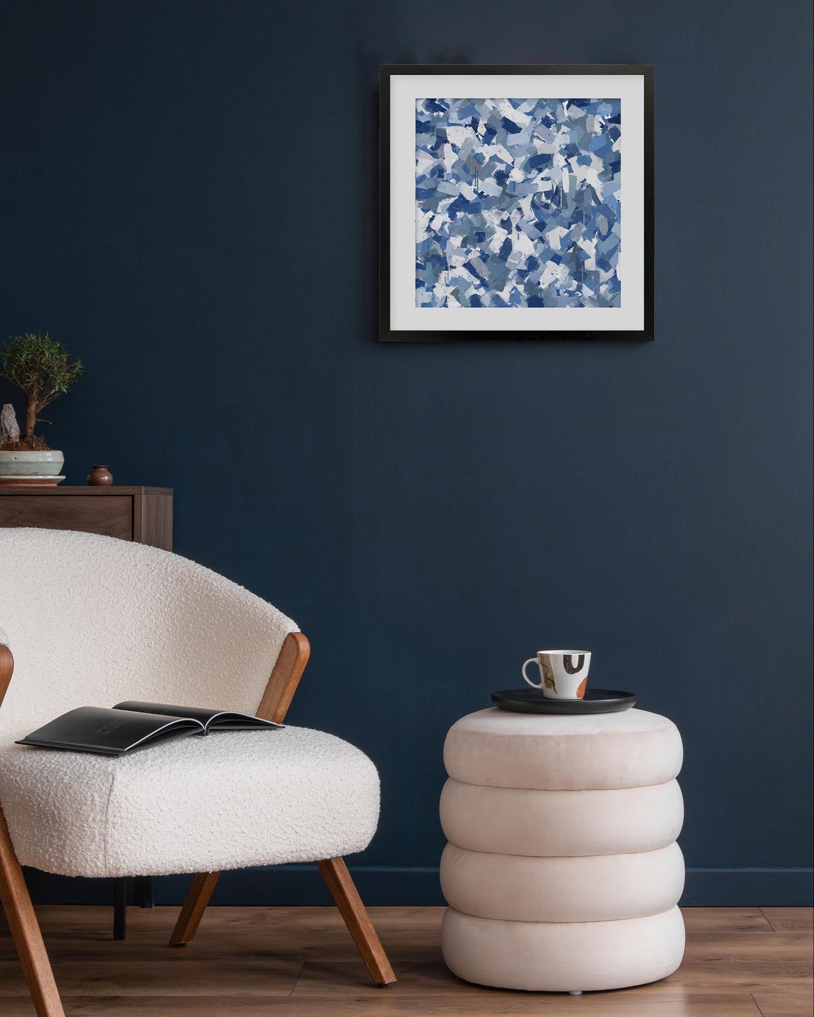 Modern living room with a textured armchair, side table, and abstract blue artwork on a dark blue wall.
