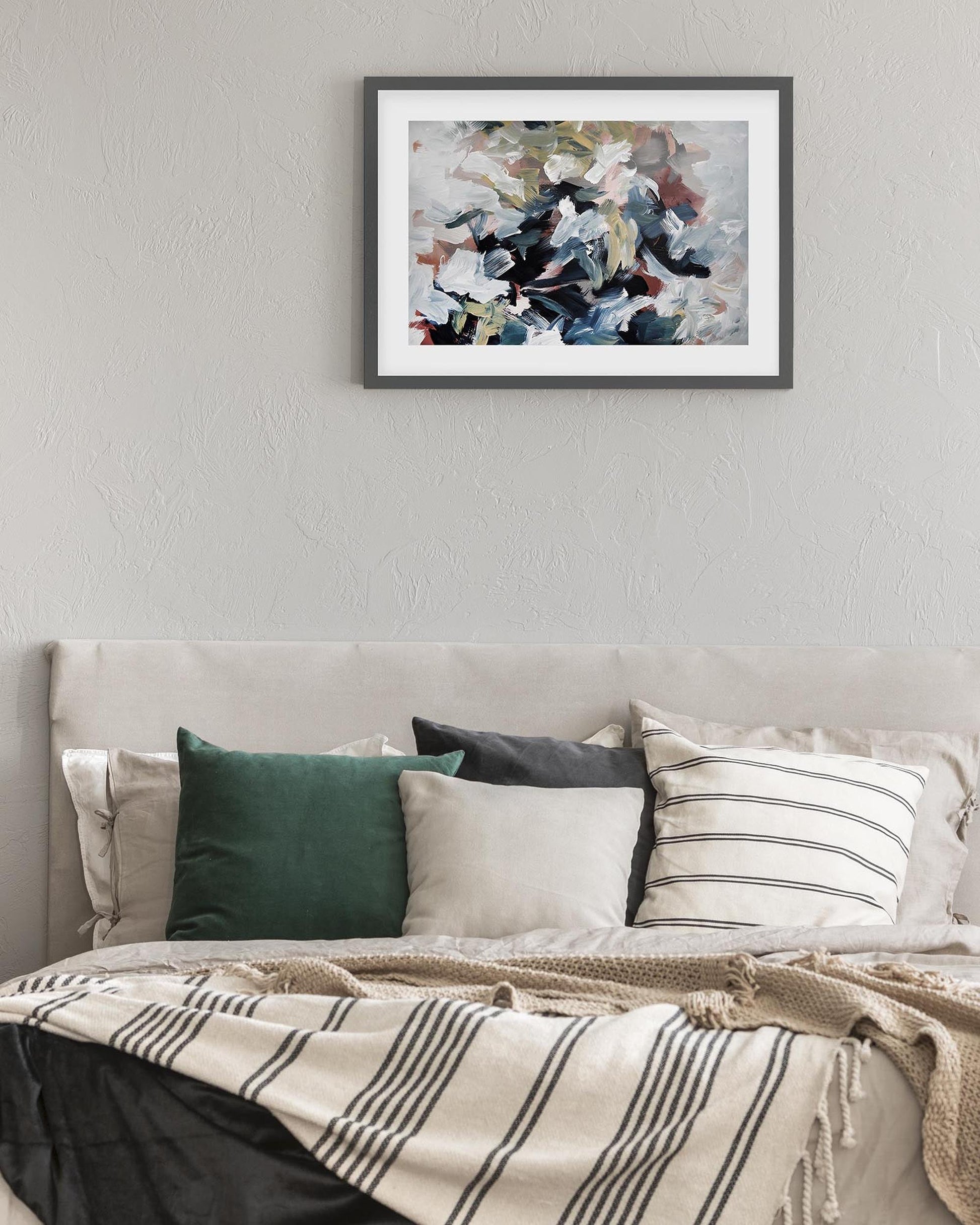 Framed abstract painting on a wall above a bed with decorative pillows.