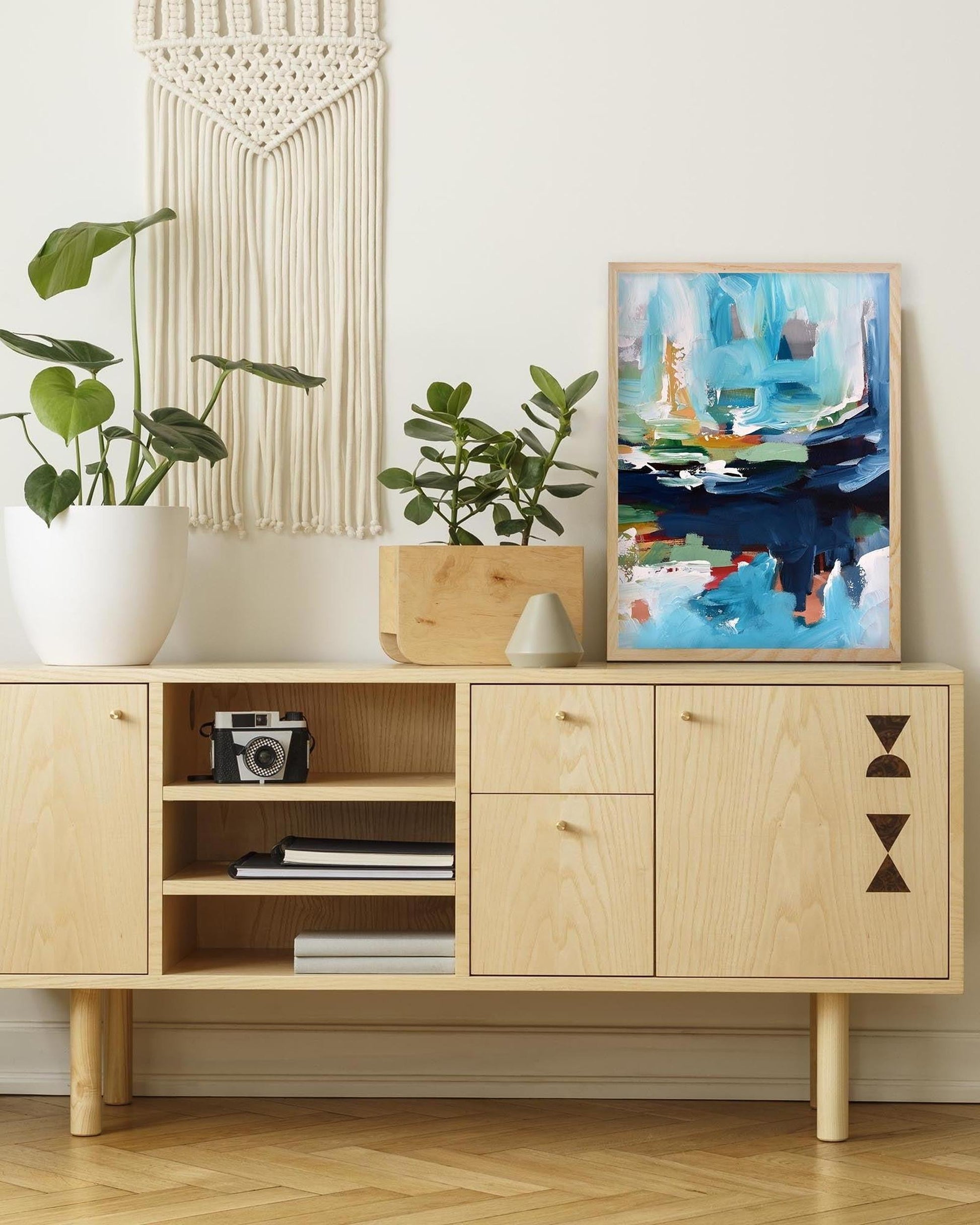 Wooden cabinet with decorative items and a framed abstract painting in a room.