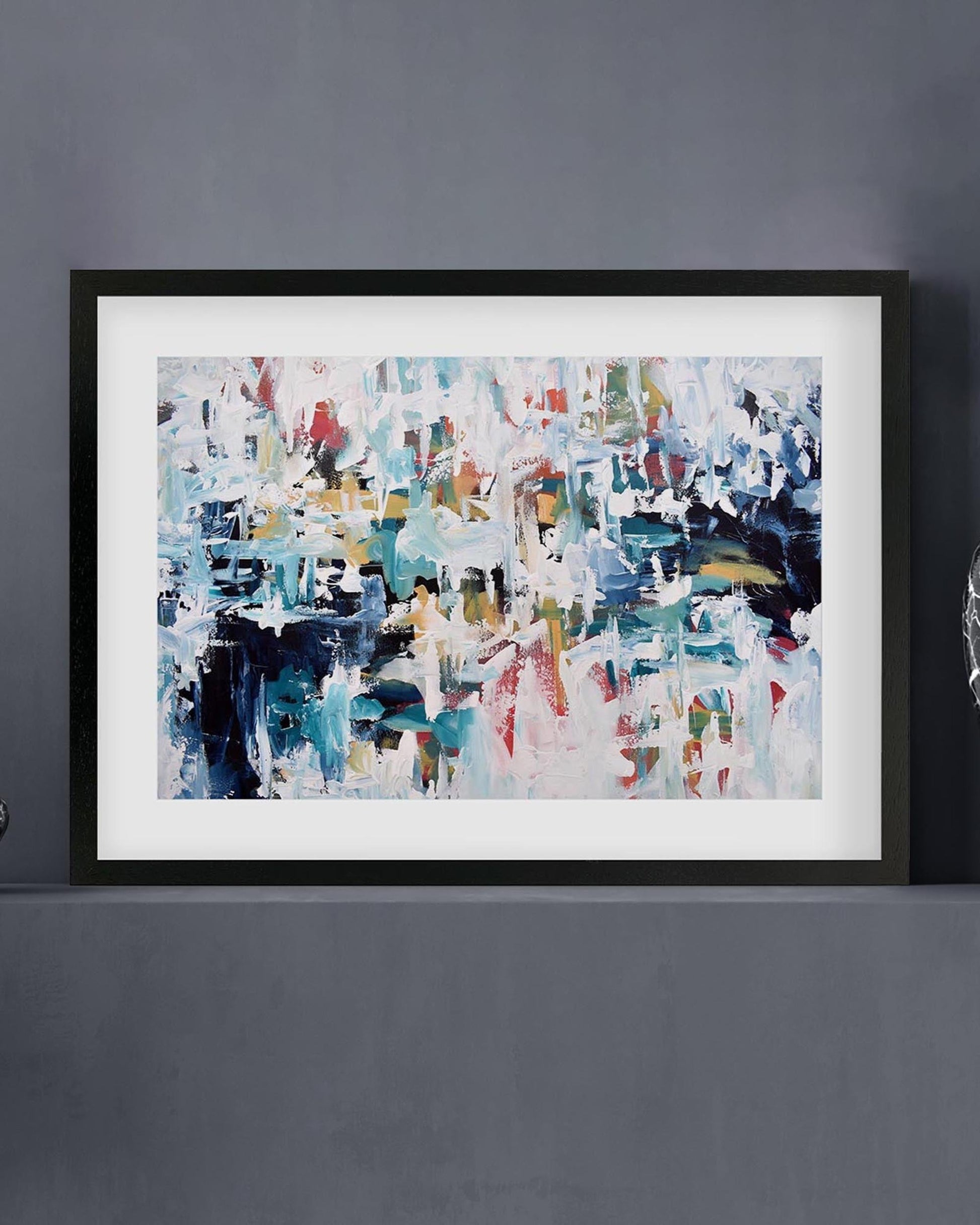 Framed abstract painting on a gray wall with decorative items.