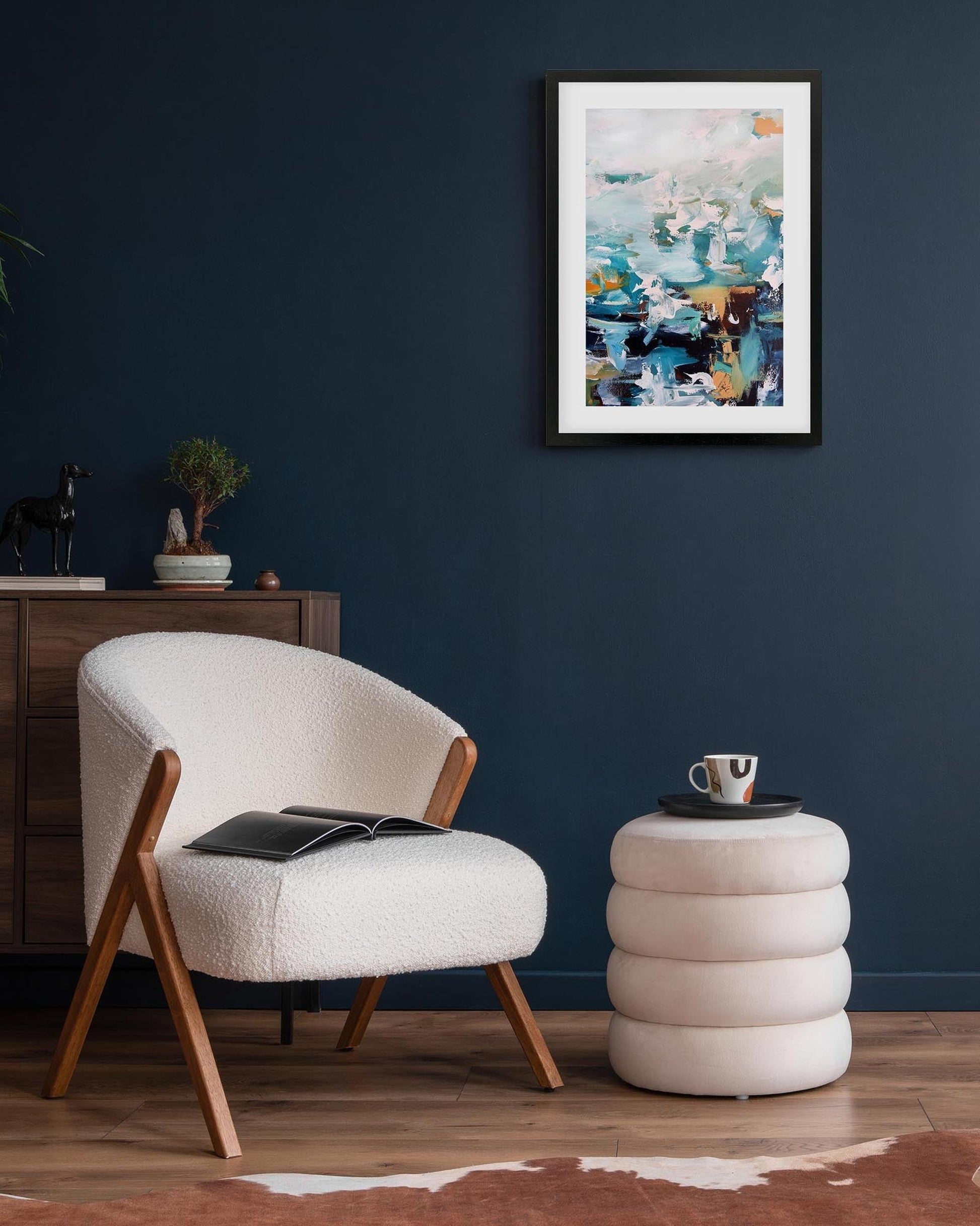 Modern living room with a white armchair, side table, and abstract painting on a dark blue wall.