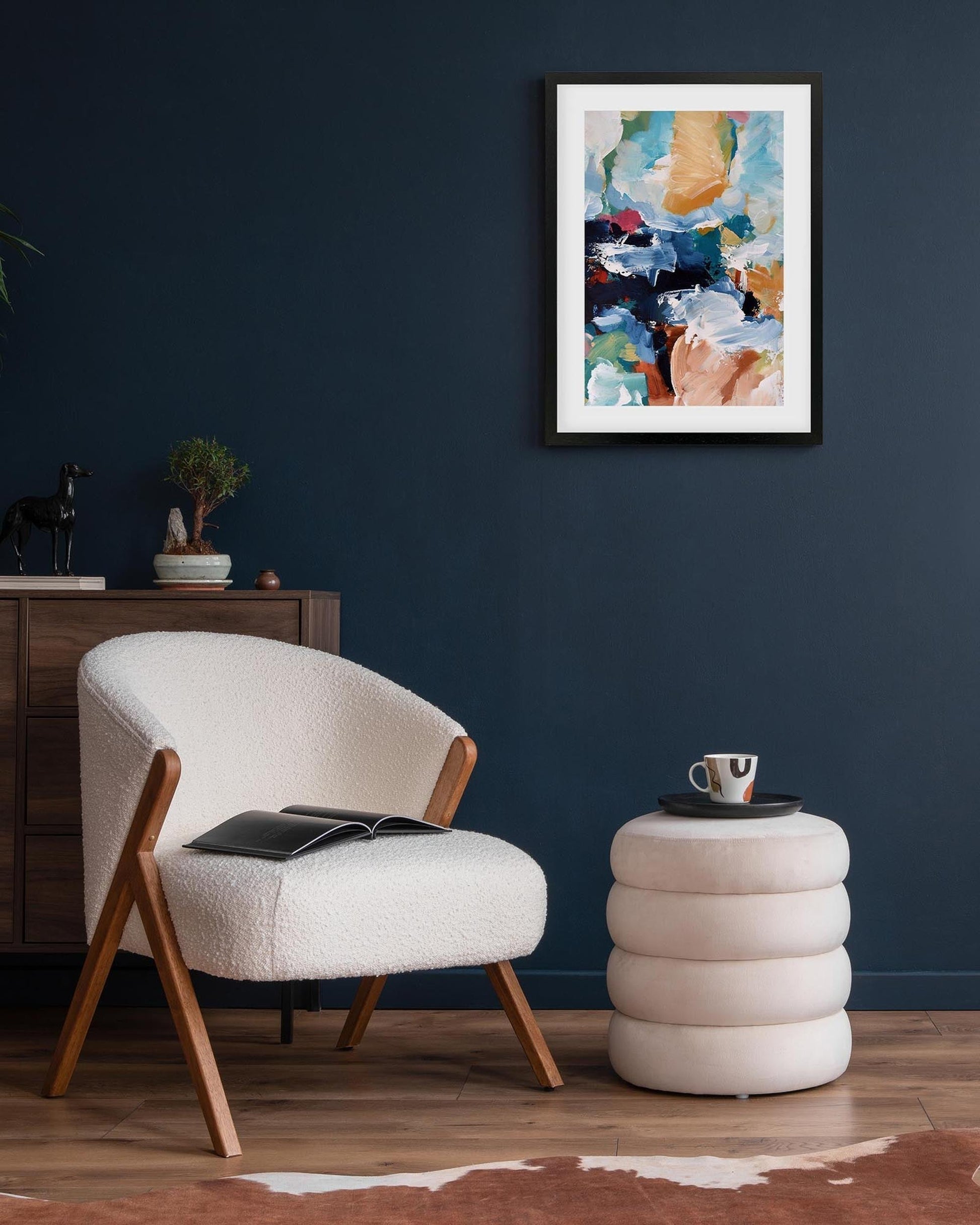 Modern living room with a white armchair, side table, and abstract painting on a dark blue wall.