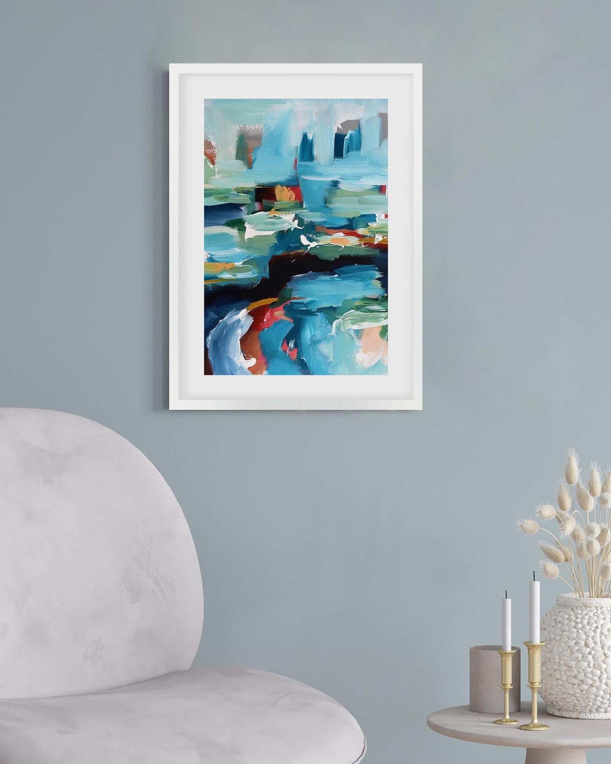 Framed abstract painting on a wall with a chair and small table in the foreground.