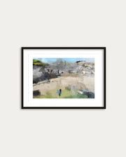 Framed artwork of a coastal village scene on a white wall