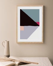 Framed abstract art print on a wall with a vase and book in the foreground.