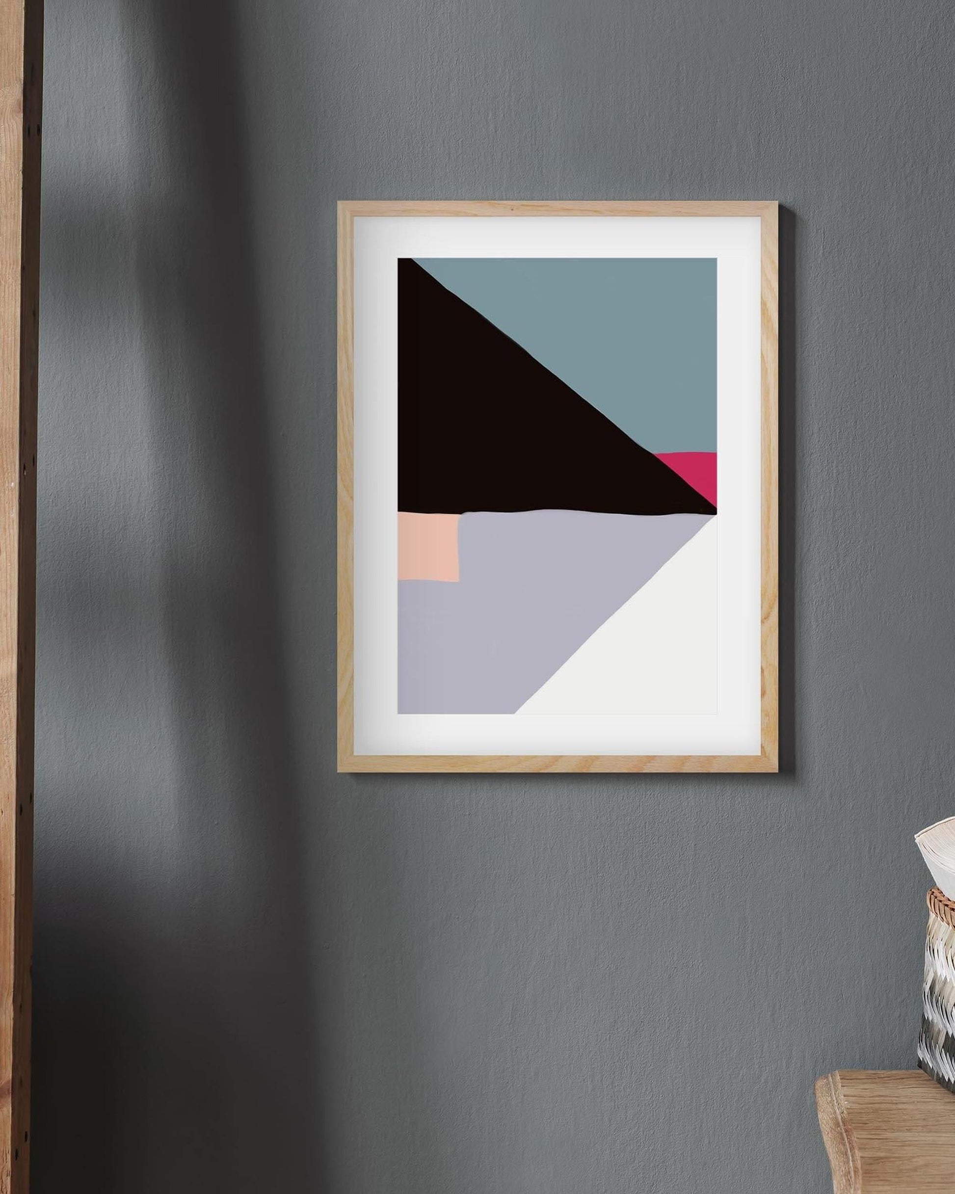 Abstract art print with geometric shapes in a wooden frame on a gray wall.