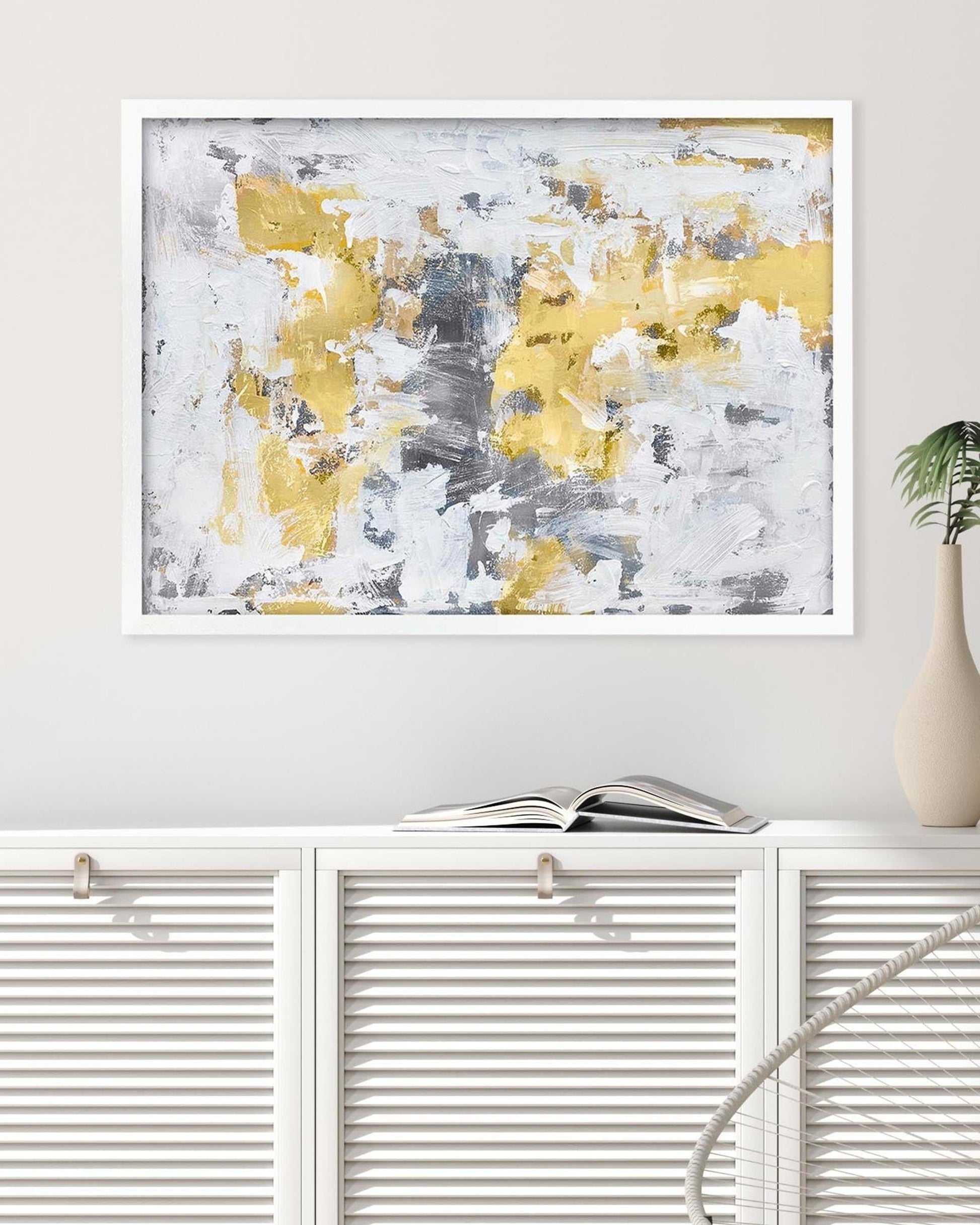 Abstract art print with yellow and gray colors in a white frame on a wall.