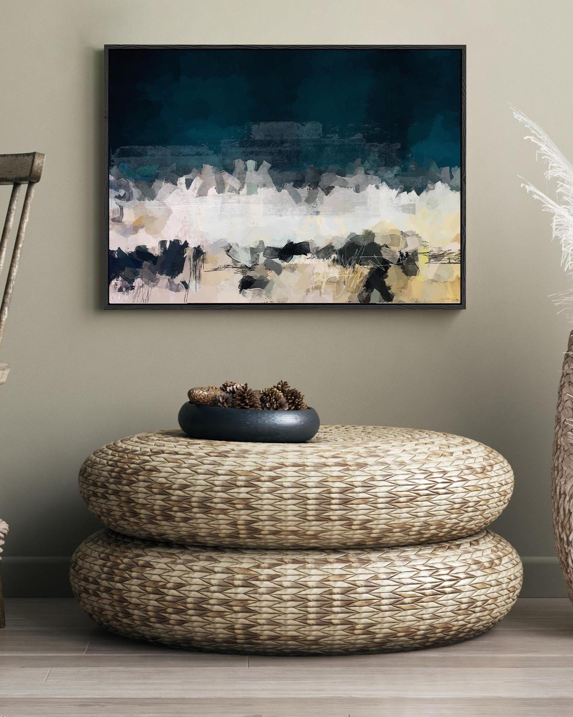 Abstract painting on a wall above a woven ottoman with decorative elements.