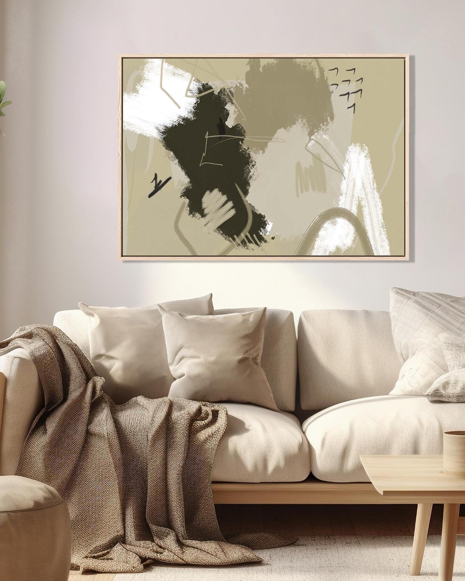 Abstract art piece on a wall above a beige sofa with a blanket draped over it.