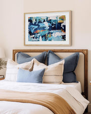 blue framed abstract art print on a wall above a bed