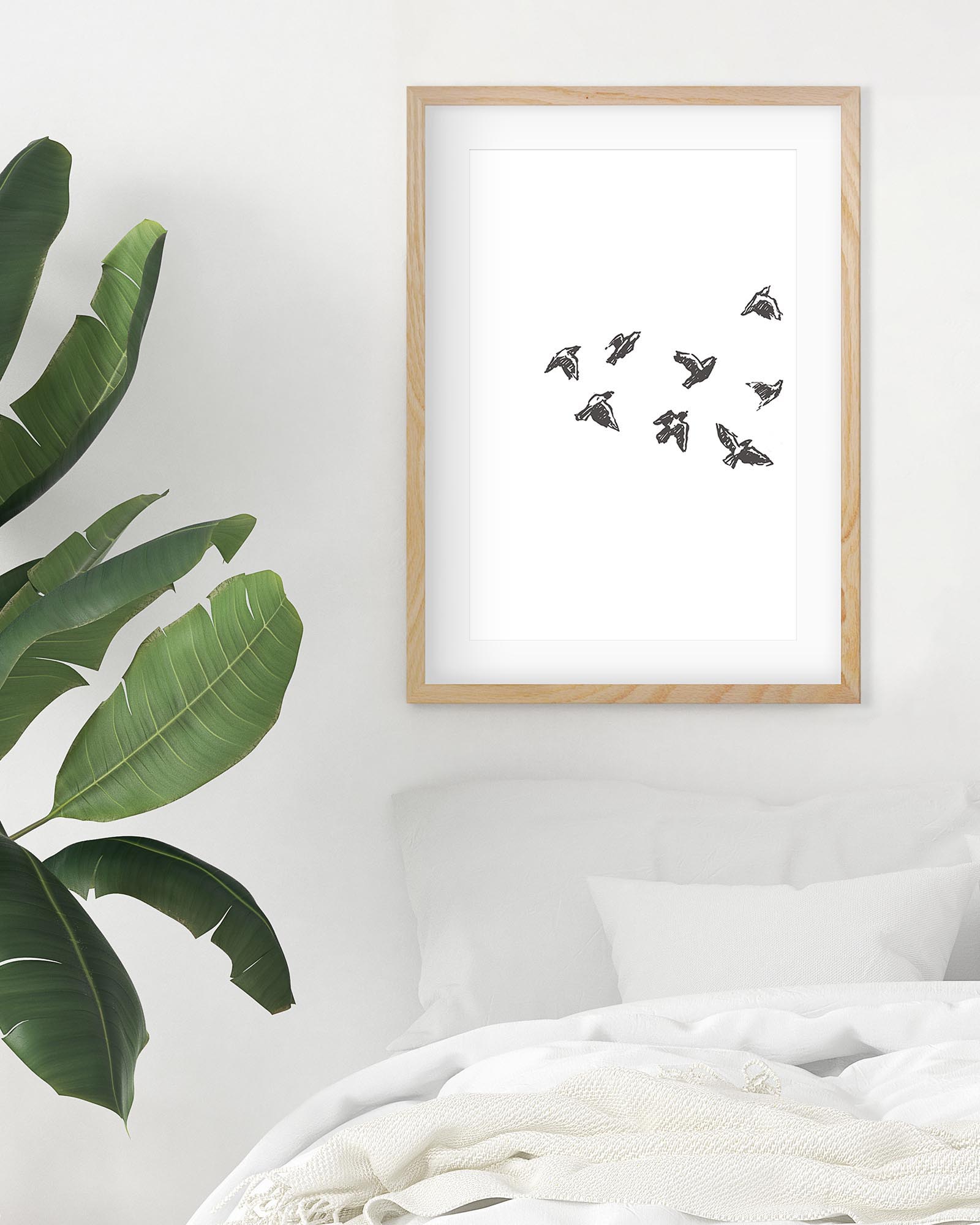 Framed artwork of birds on a white wall with a plant to the left.