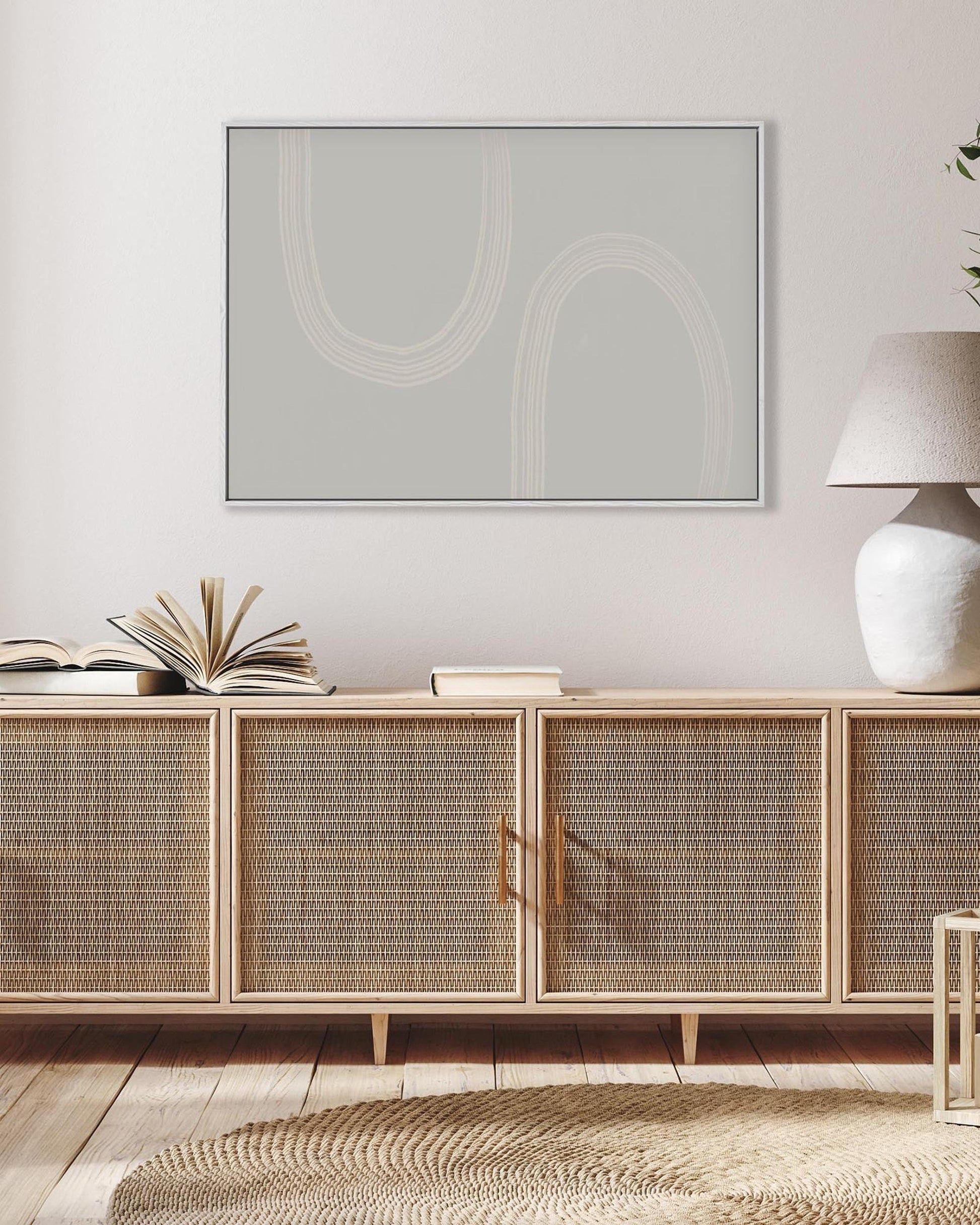 Wicker cabinet with books and a lamp in a room with a framed abstract painting on the wall.