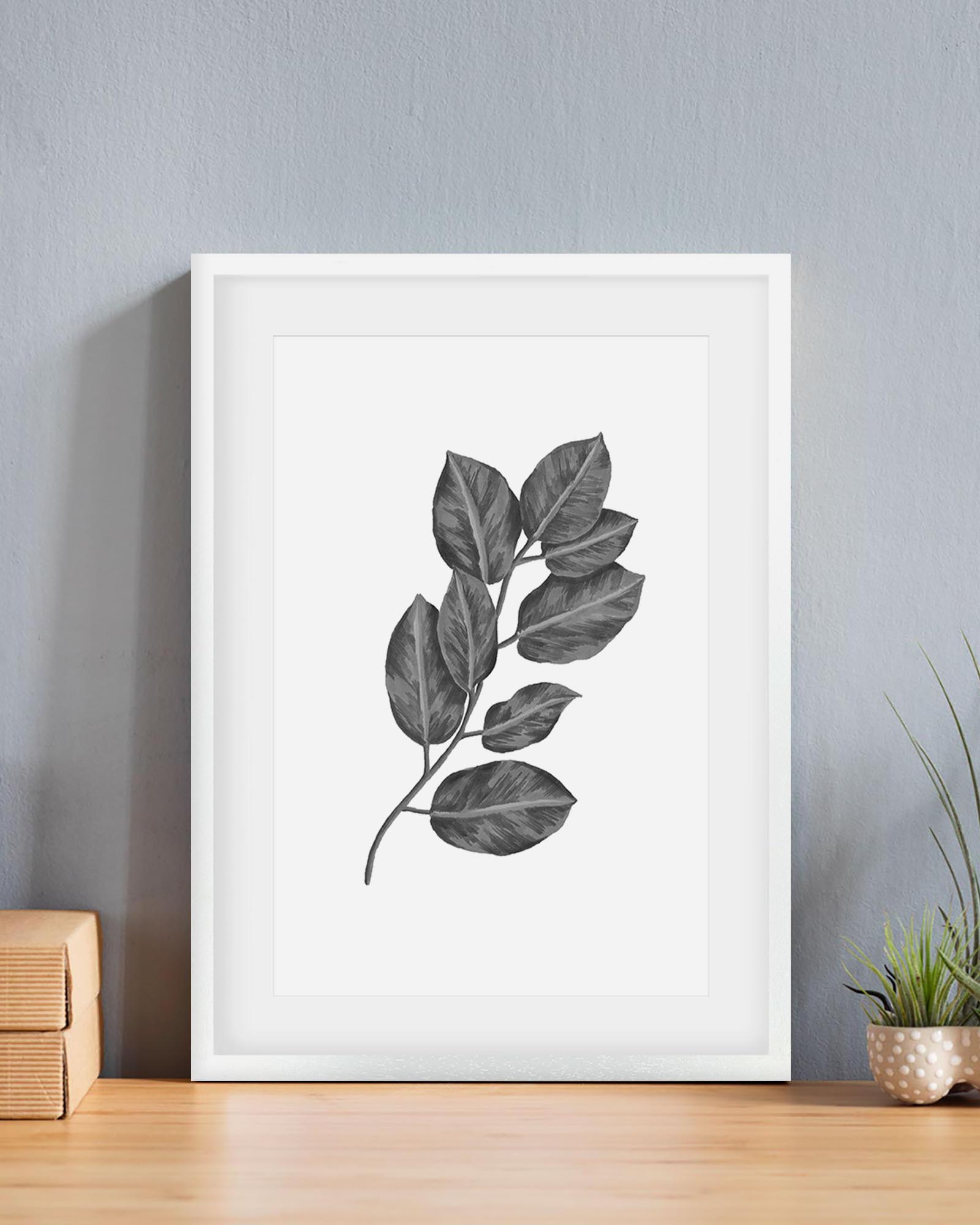 Framed artwork of a leaf design on a wall with a plant and wooden box in the background.