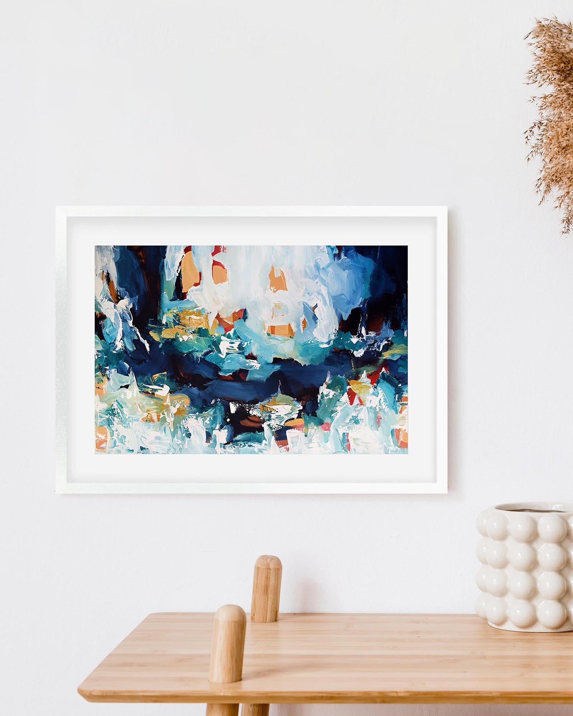 Framed abstract art print on a wall above a wooden table