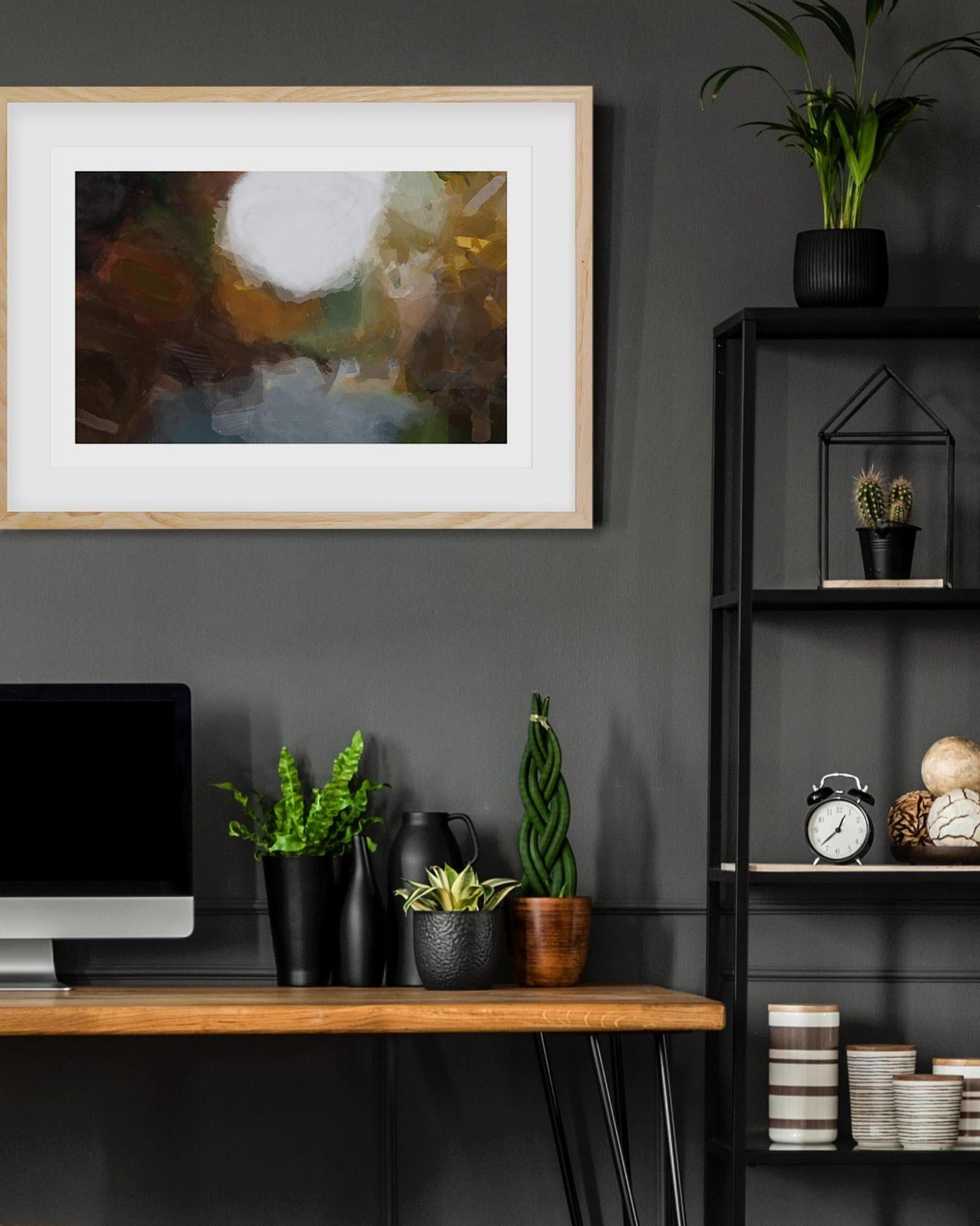 Modern office space with a framed abstract painting, plants, and a computer on a desk.