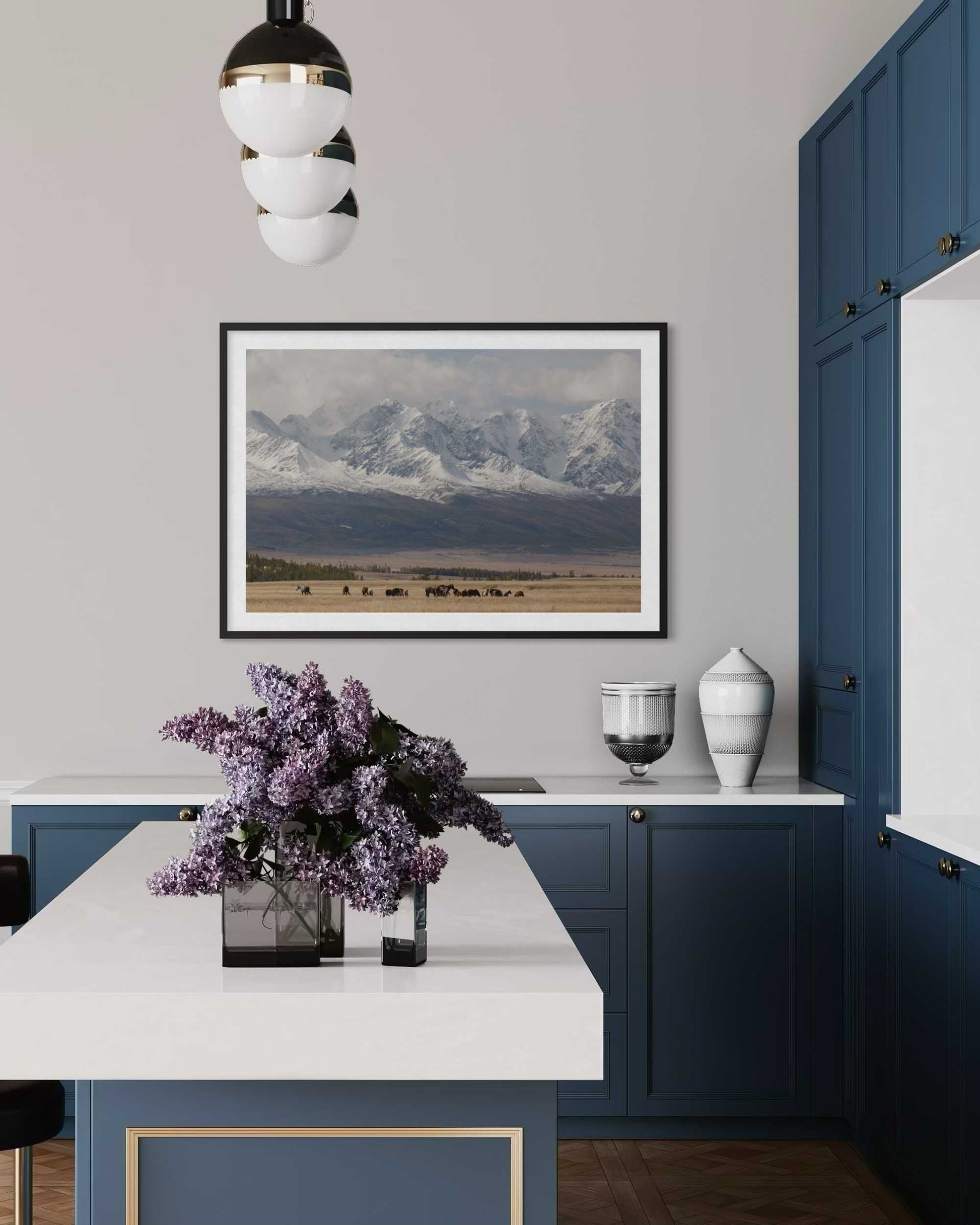 Modern kitchen with blue cabinets, white countertops, and a mountain landscape print on the wall.
