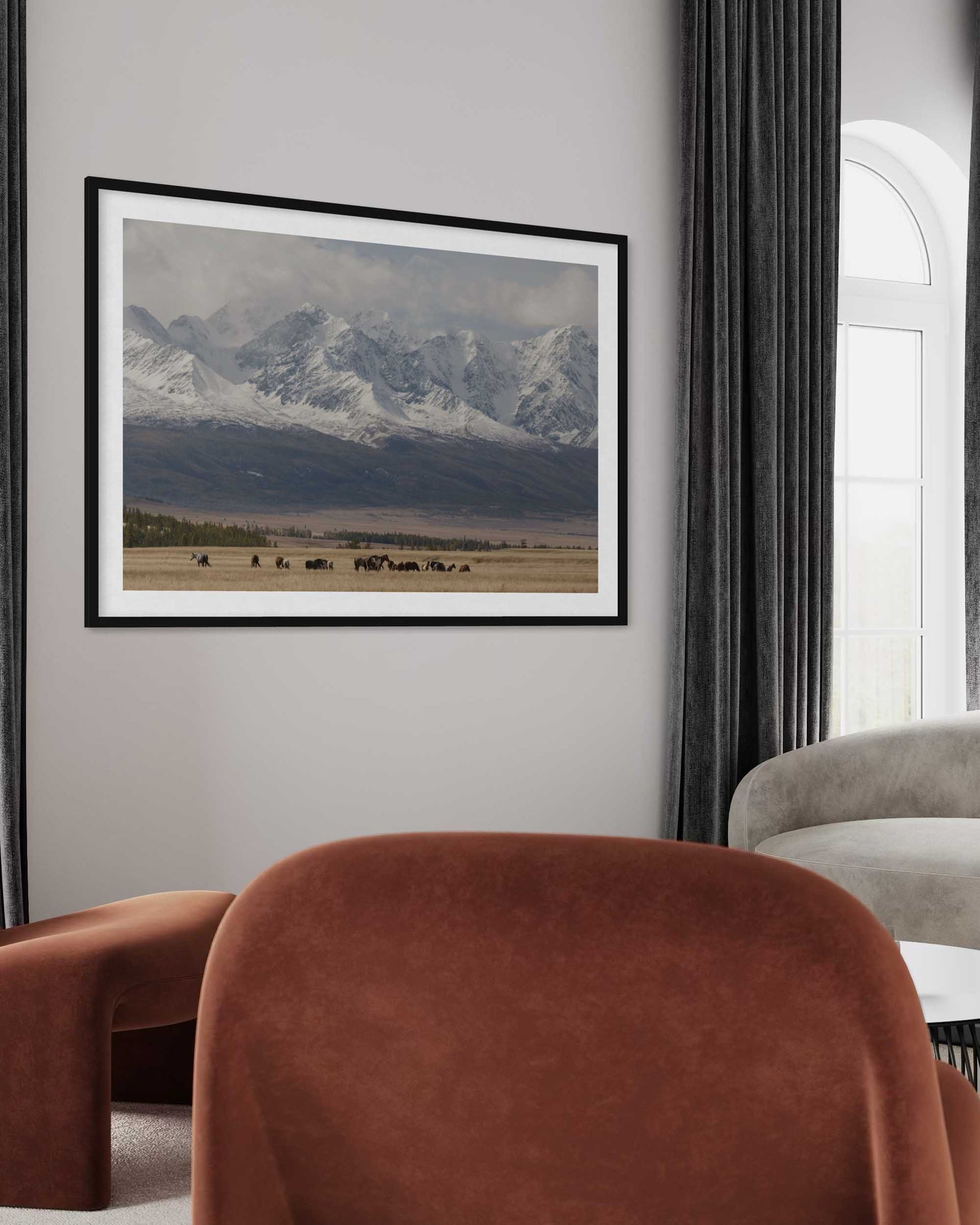 Framed landscape print of mountains on a wall in a living room with brown chairs.
