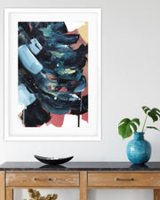 Framed abstract art piece on a wall above a wooden console table with decorative items.