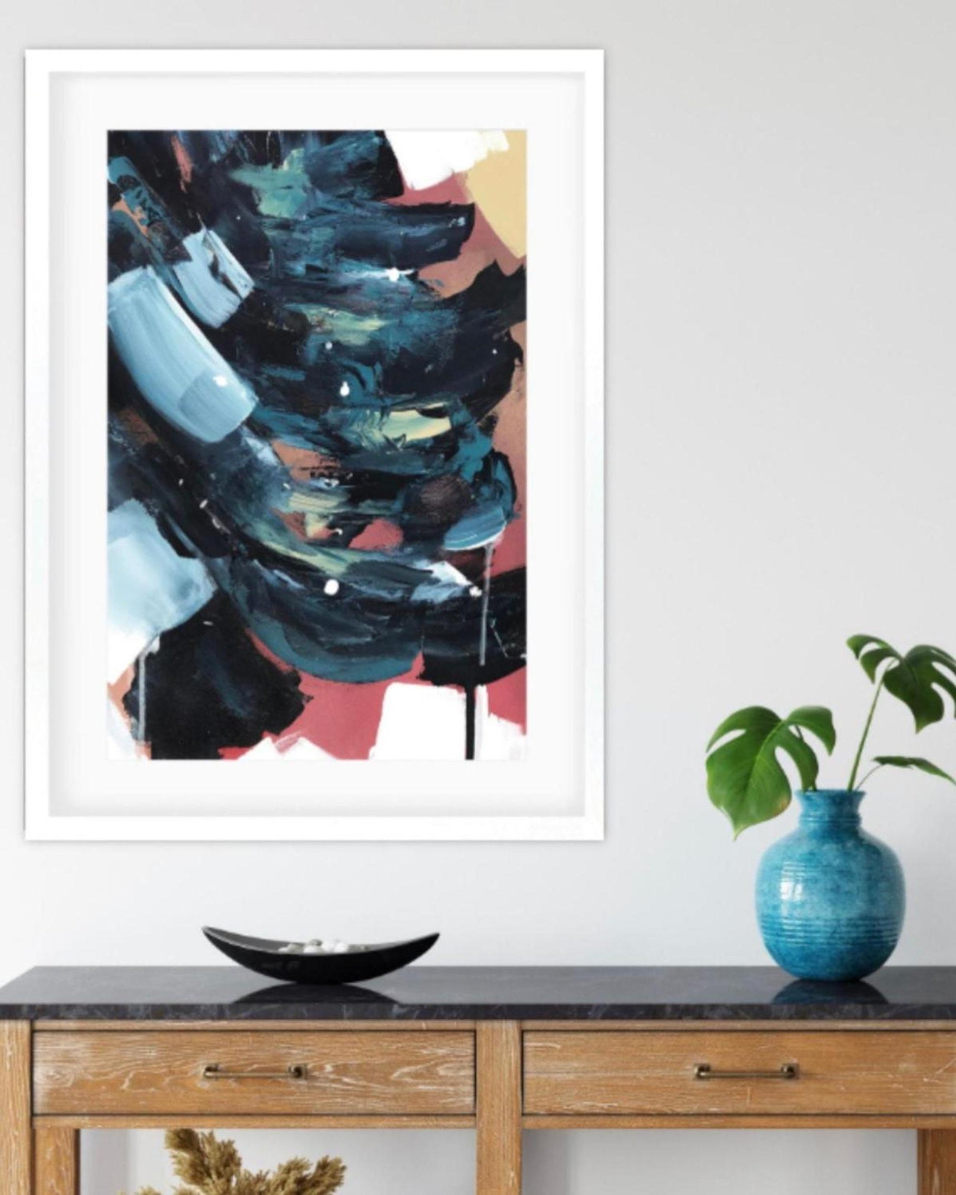 Framed abstract art piece on a wall above a wooden console table with decorative items.
