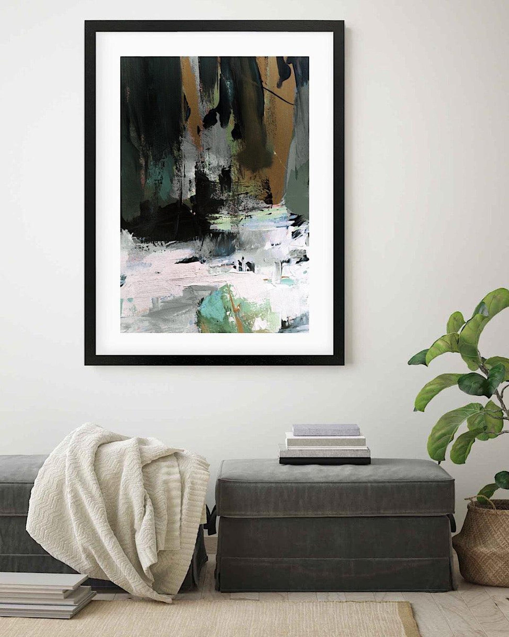 Framed abstract art piece on a wall above a bench with books and a blanket.