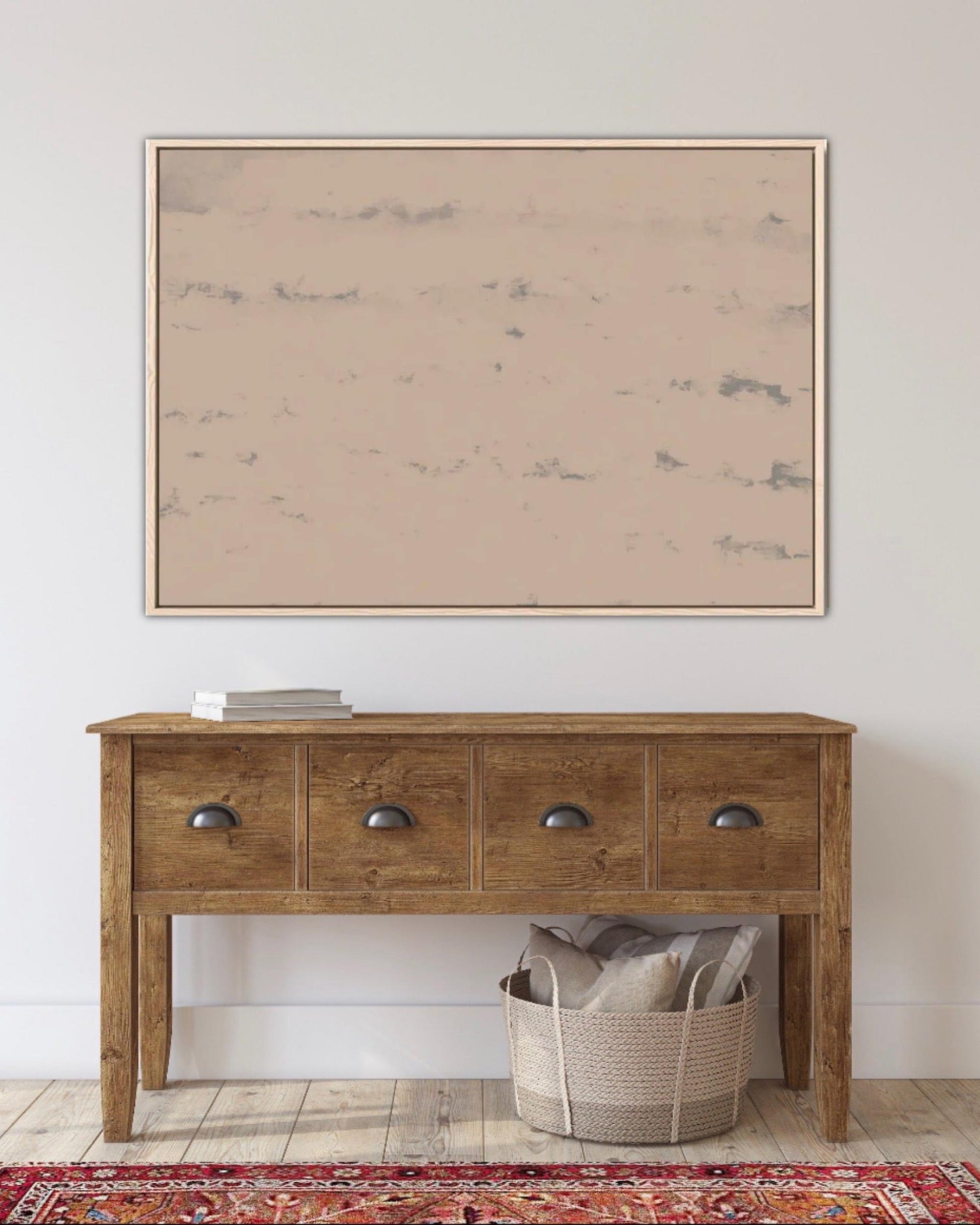 Wooden console table with a basket and pillows underneath, framed artwork above on a white wall.