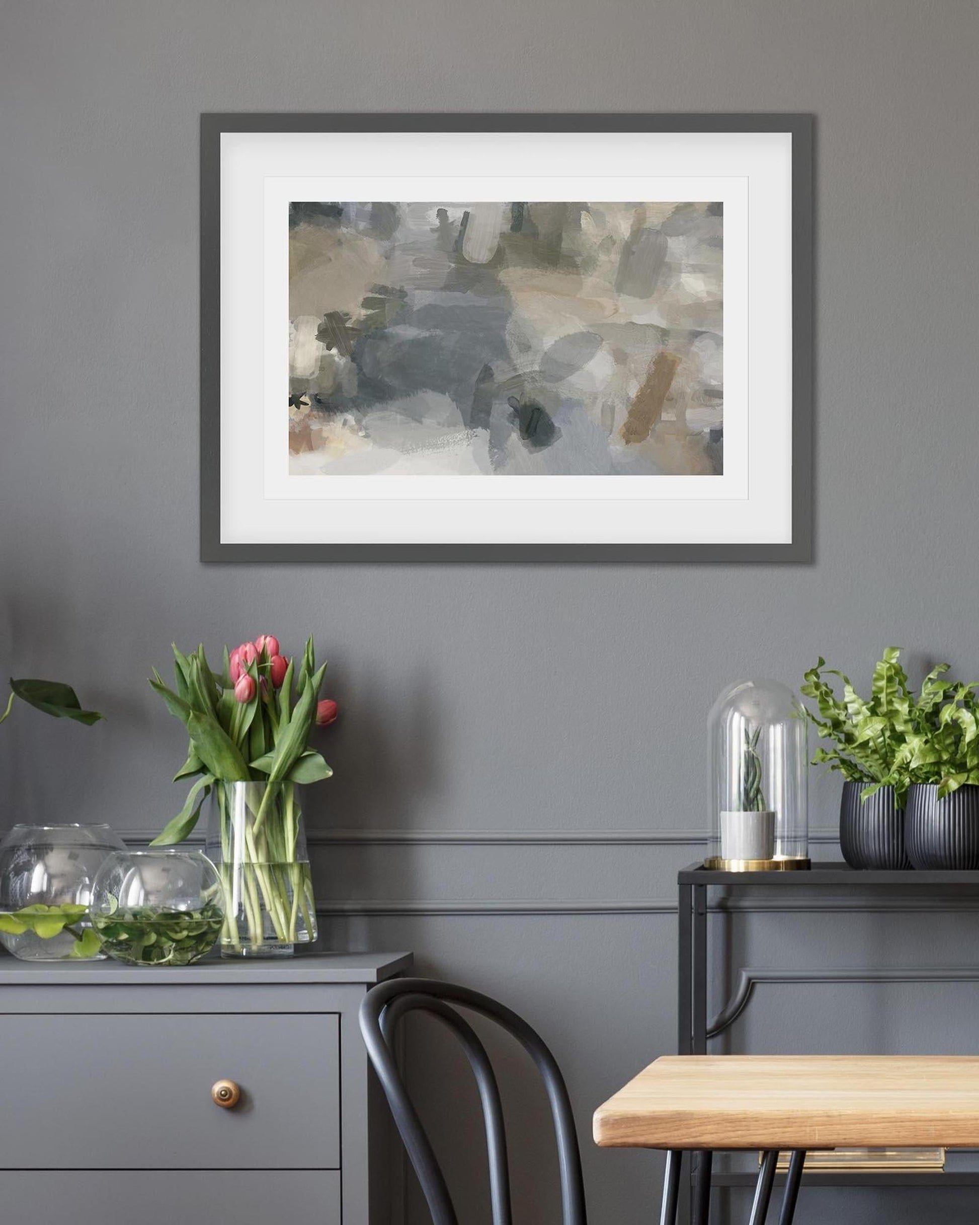 Framed abstract painting on a gray wall with decorative elements below.