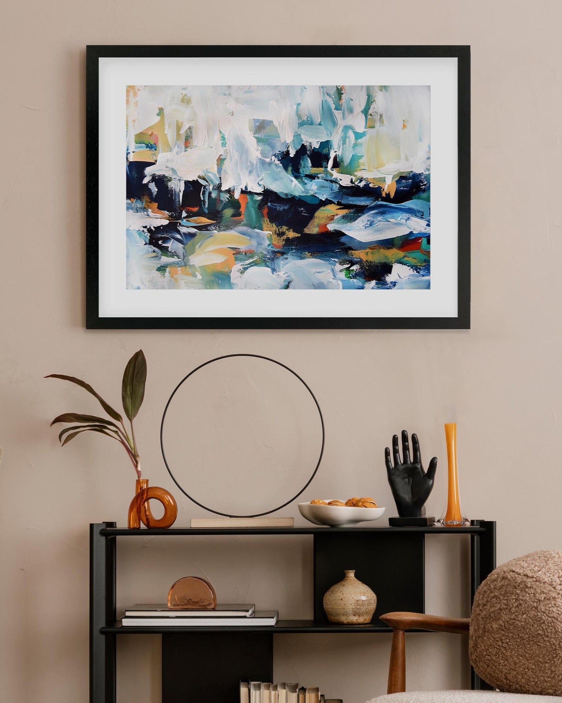 Framed abstract painting on a wall above a shelf with decorative items.