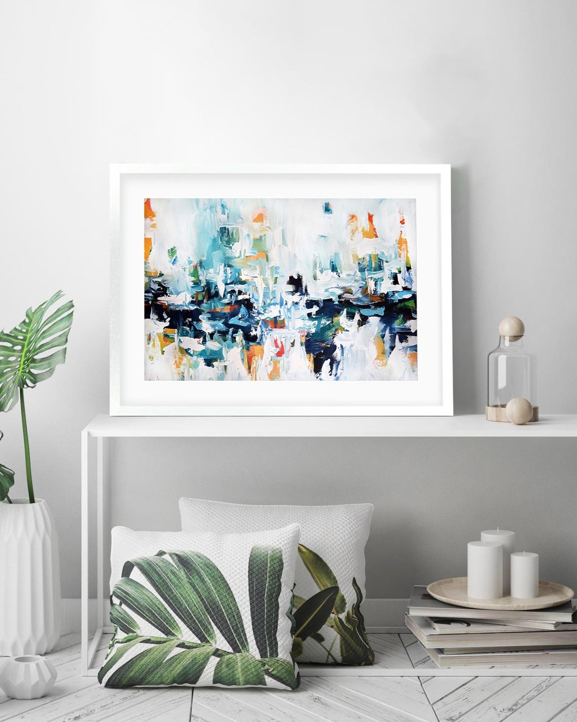 Framed abstract art piece on a shelf with decorative items including a plant and candles.