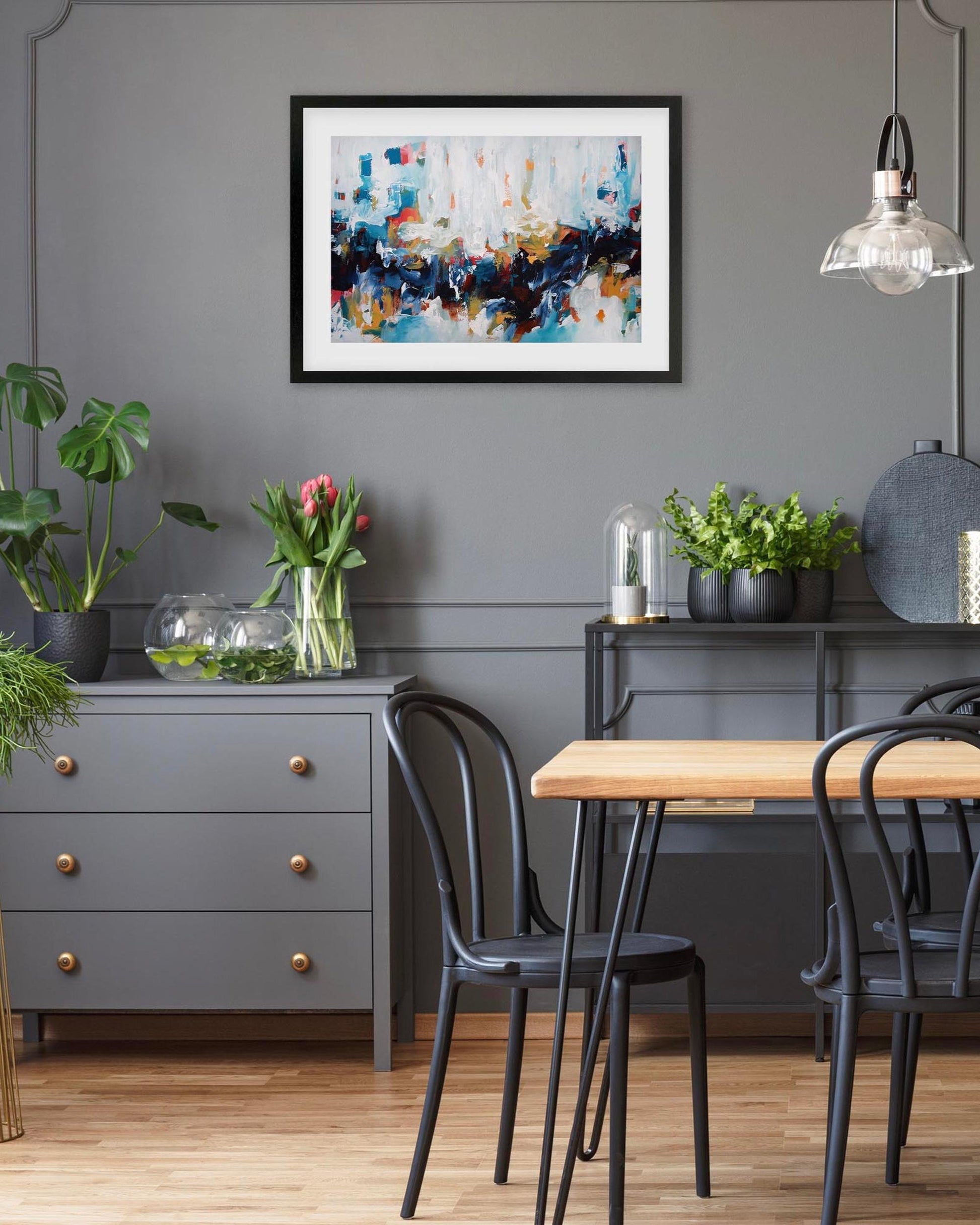 Dining room with a gray wall, abstract art, plants, and a wooden table.
