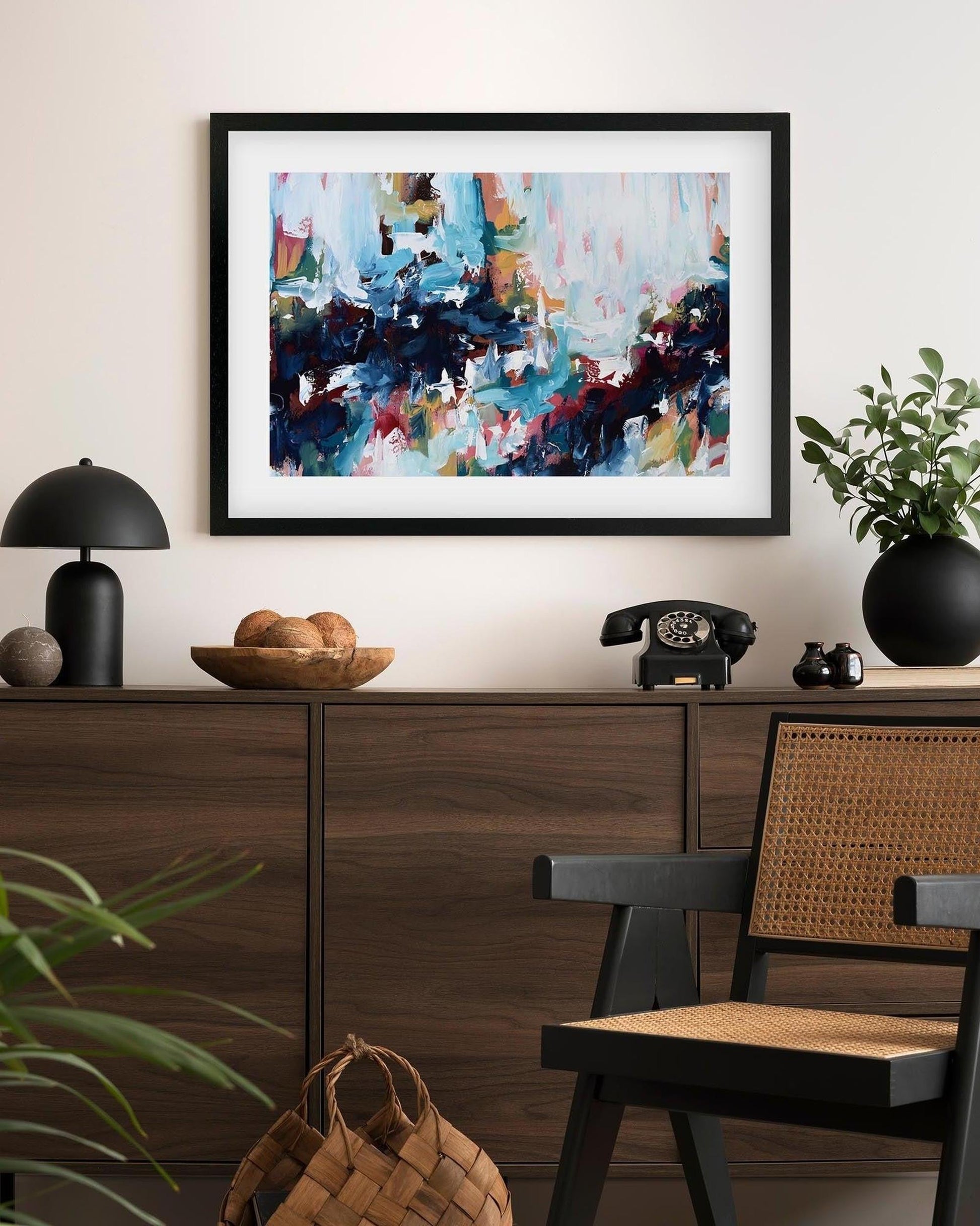 Abstract art piece in a black frame on a wall above a wooden console table.
